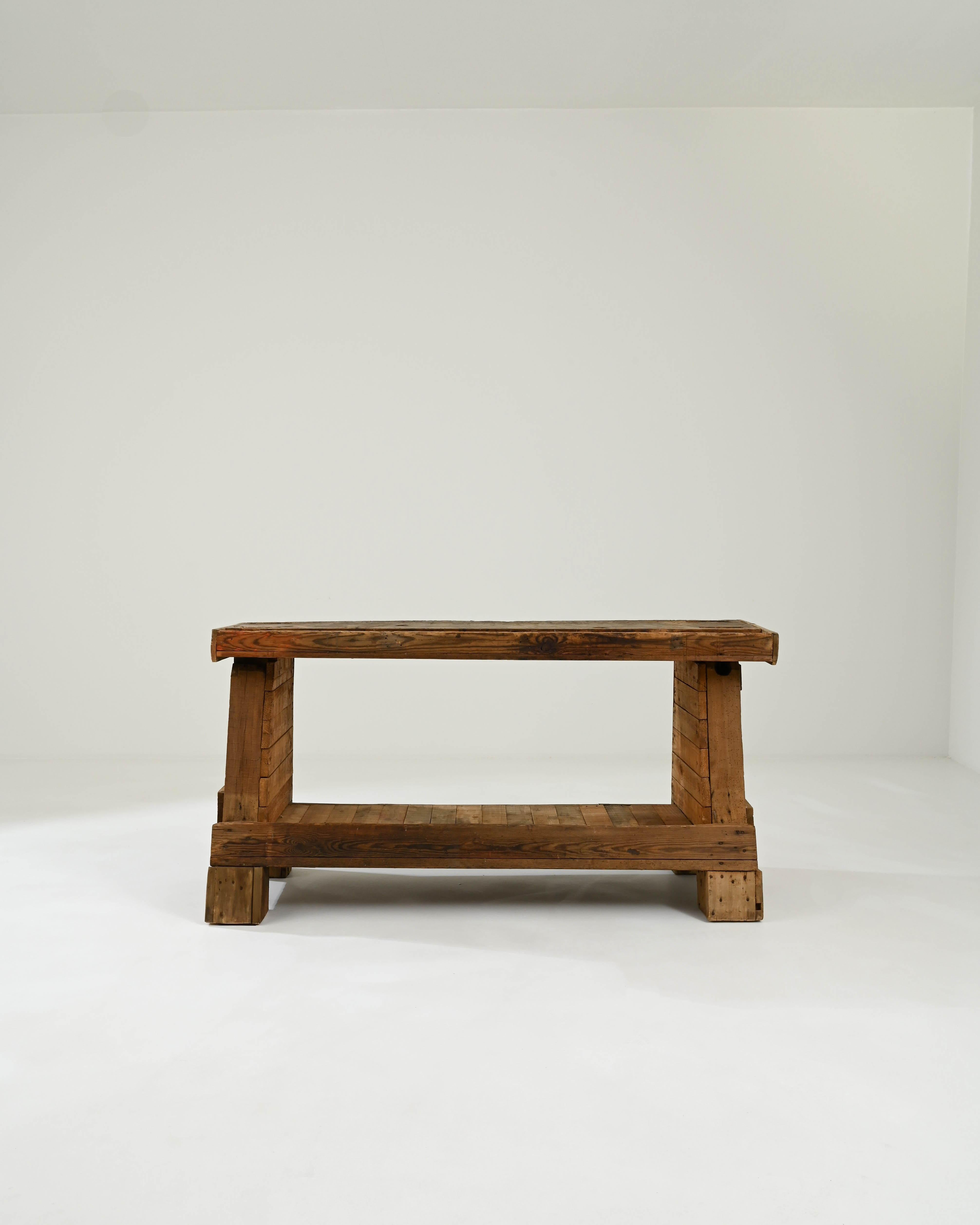 Built in the early 20th century, this charming antique work table stands on sturdy A-shaped legs with large square feet for added support. The long, narrow table top features a deep trough that can be used for storing tools. Beneath, a lower shelf