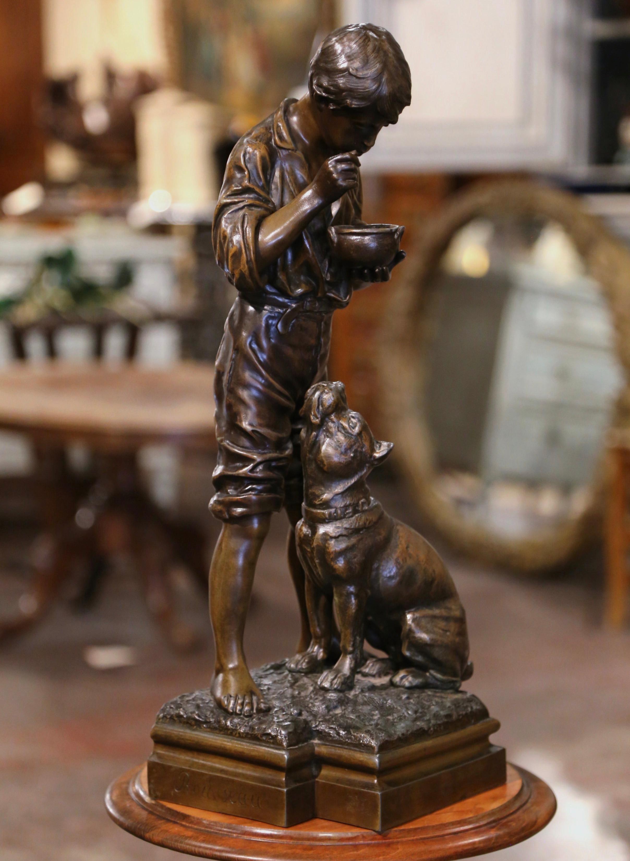 Place this tall patinated sculpture on a console or a buffet! Crafted in Belgium in 1932, the metal statue depicts a young boy eating his bowl of soup with dog watching with envy. The figurine has numerous marking to prove authentication. It is