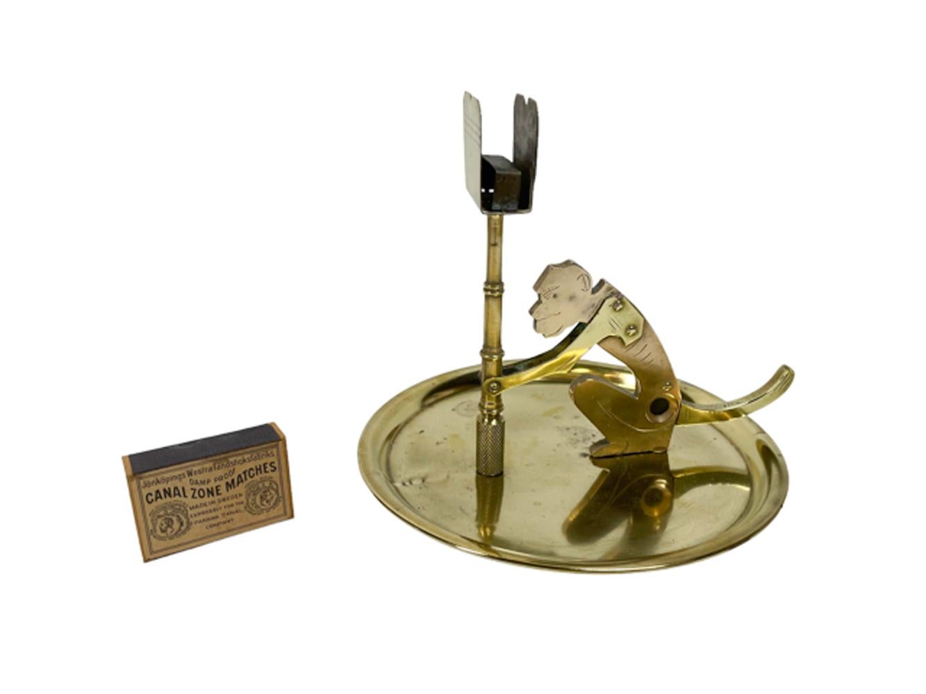 Early twentieth century cigar cutter in the form of a monkey holding a lamp post which holds a match box, on a circular ashtray base. The body of the monkey is bell metal (brass with high copper content, giving it a pinker color)), the rest is
