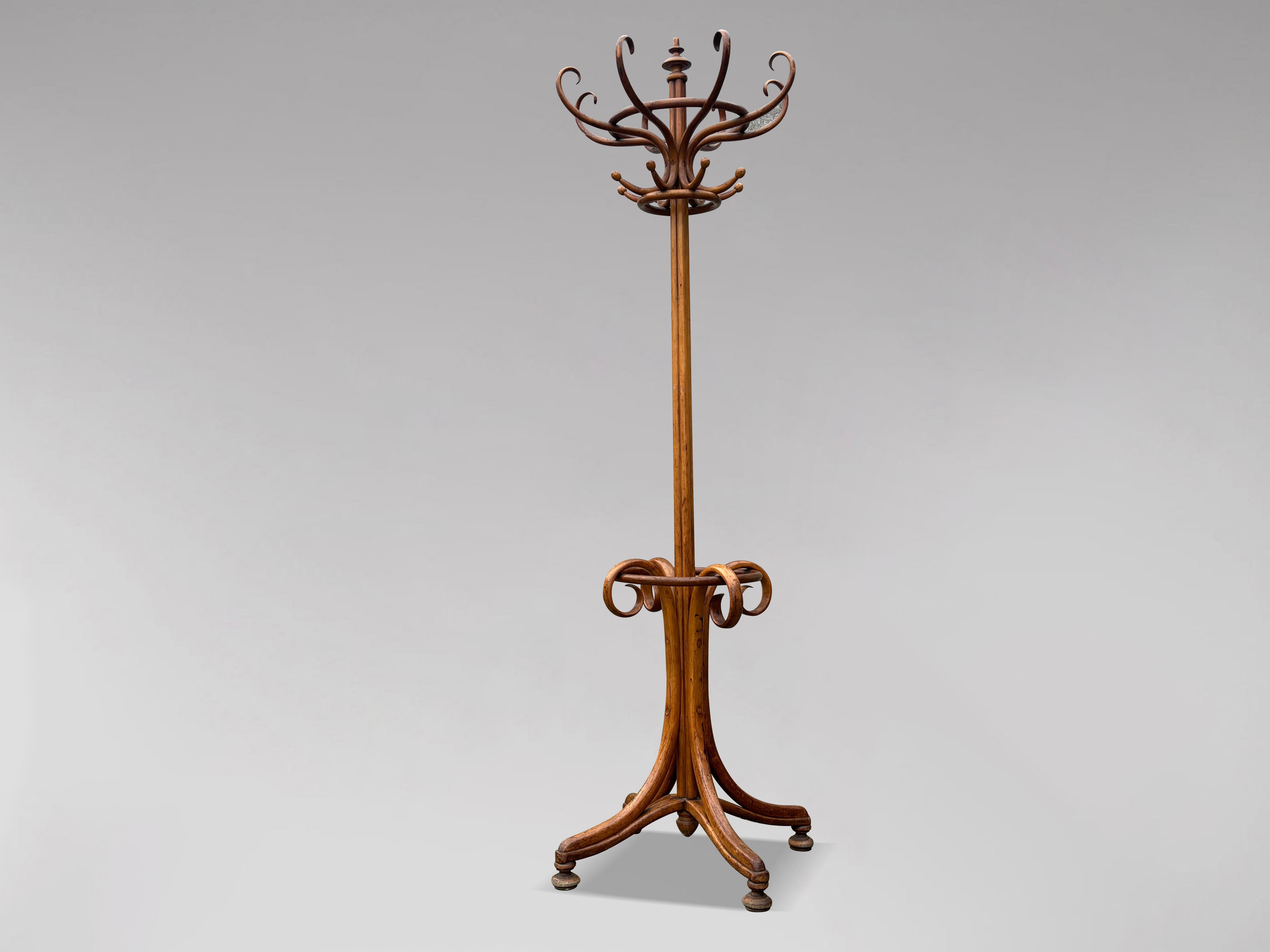 Ein antiker Mantel- und Hutständer aus Bugholz in der Art von Thonet aus dem frühen 20. Jahrhundert. In der Mitte befindet sich ein kleiner, gedrechselter Abschluss, der stolz über der Struktur steht, sowie acht schlangenförmige Kleiderhaken mit