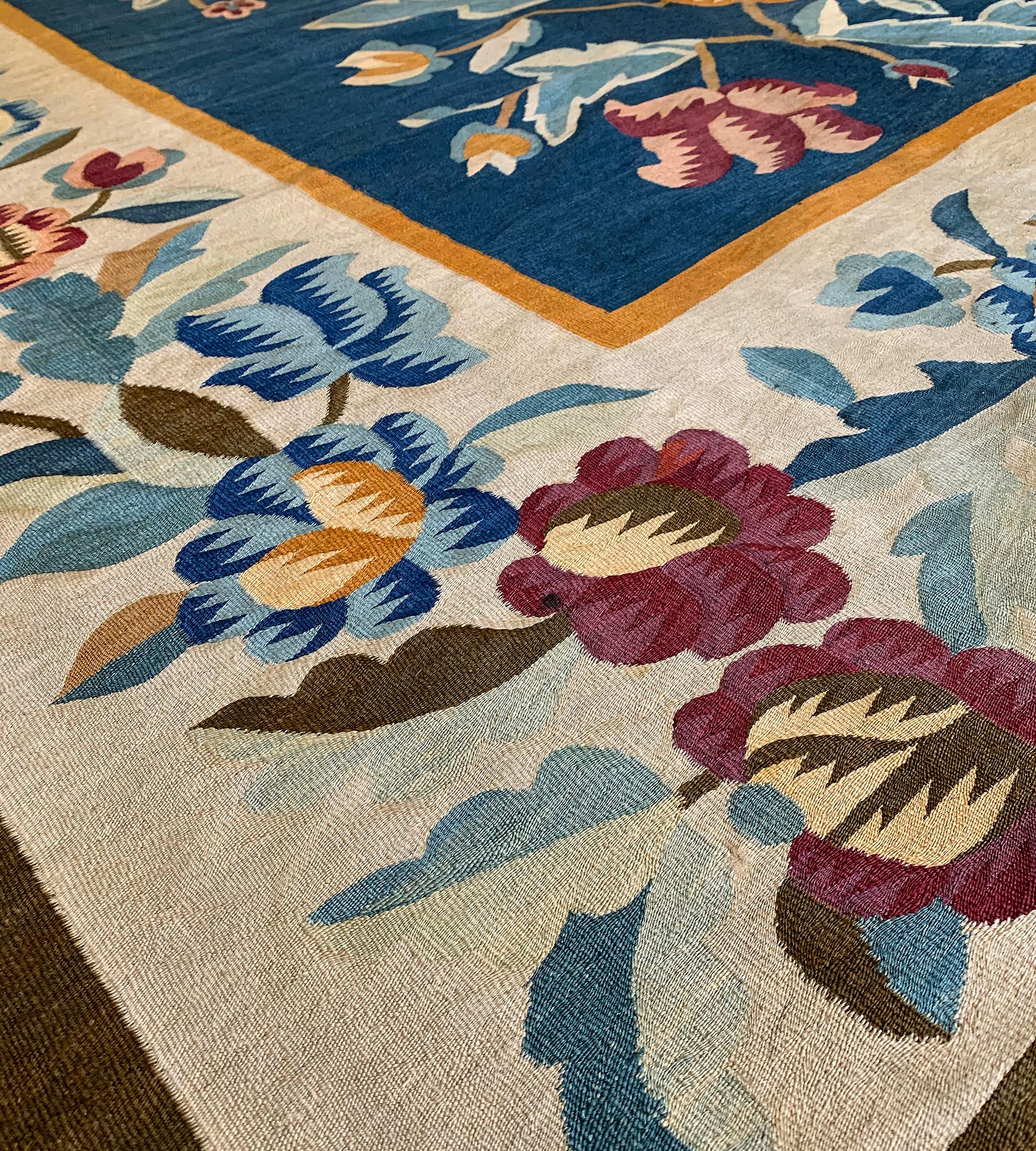 This antique traditional handwoven Romanian Bessarabian rug has a medium-blue field with three large polychrome floral sprays, in a beige border of linked flowerhead vines between plain delicate stripes.