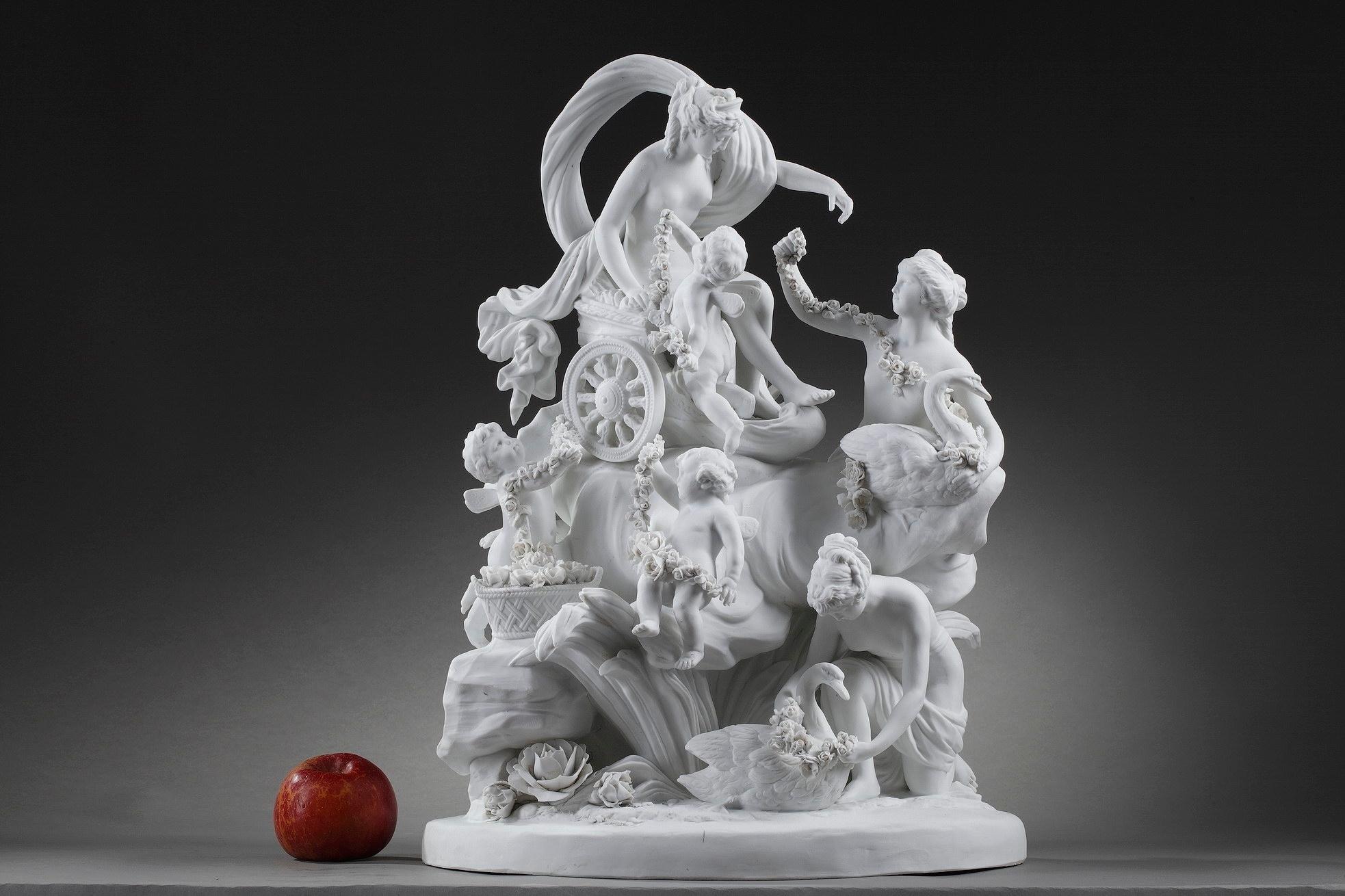 Large porcelain bisque group featuring the triumphant figure of the goddess Aphrodite (Venus) on her chariot, surrounded by Cupids and Nereids with swans. The nymphs and putti reach to the goddess garlands of roses as symbol of glory. Two Cupids in