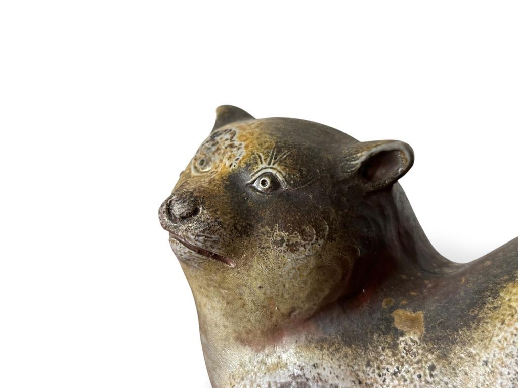 Una escultura de perro de cerámica encantadora y con carácter, elaborada según la célebre tradición de la cerámica Bizen de Japón. Fechada a principios del siglo XX, esta expresiva pieza representa un perro agazapado con finos detalles y una cálida