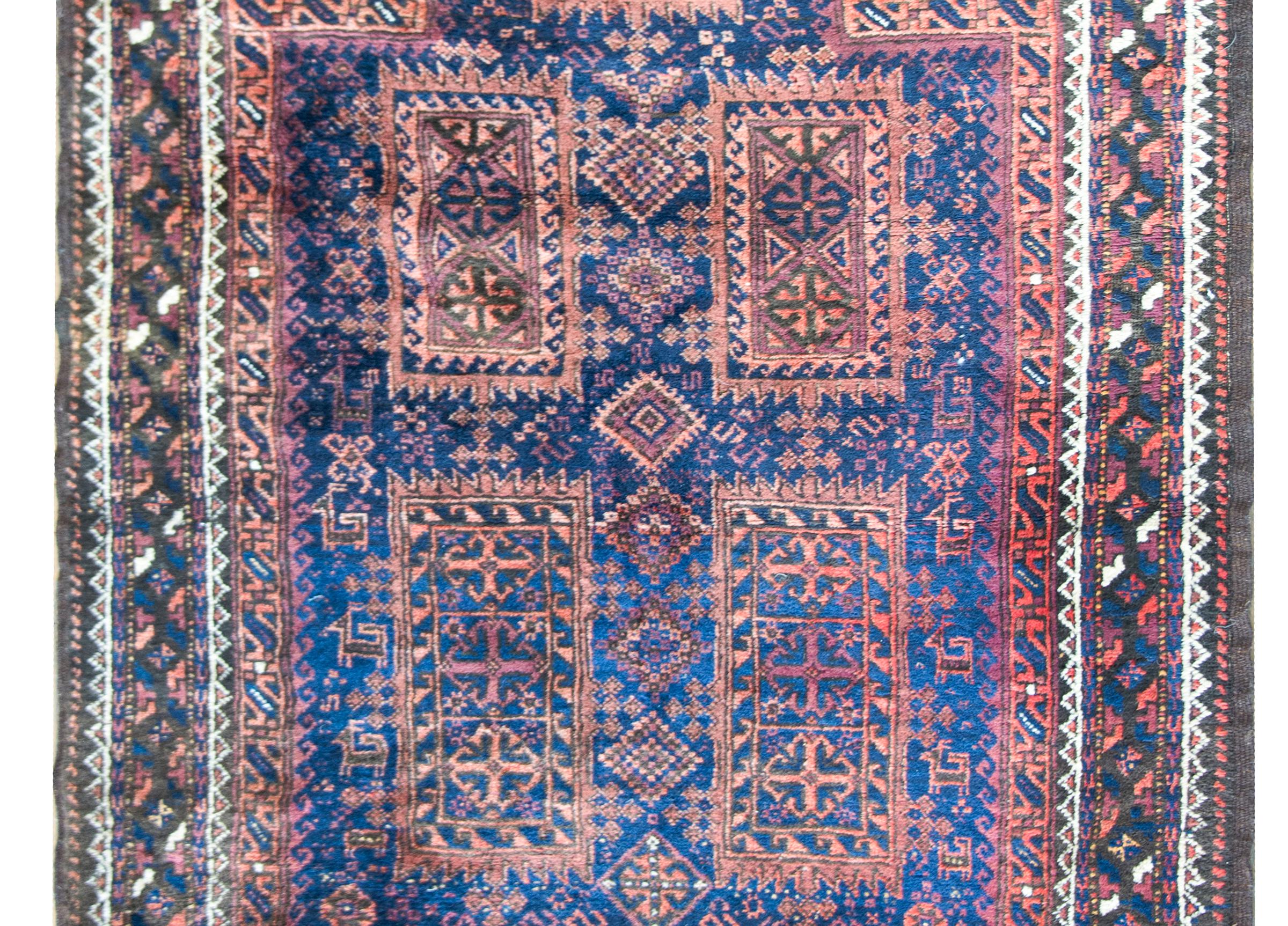 A wonderful early 20th century Persian Bluchi prayer rug with an all-over geometric and stylized floral pattern and surrounded by a complex border of multiple geometric patterned stripes, and all woven in indigo, orange, brown and white wool.