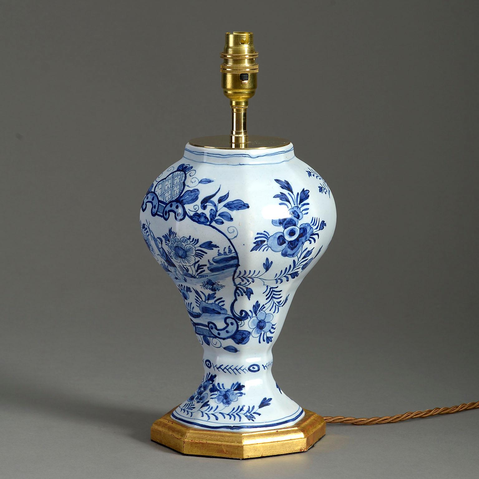 An early twentieth century blue and white glazed Delft pottery vase, of hexagonal baluster form and decorated throughout with chinoiseries. Now mounted as a lamp on a water gilded base.

Dimensions refer to vase and base only.

Wired to UK