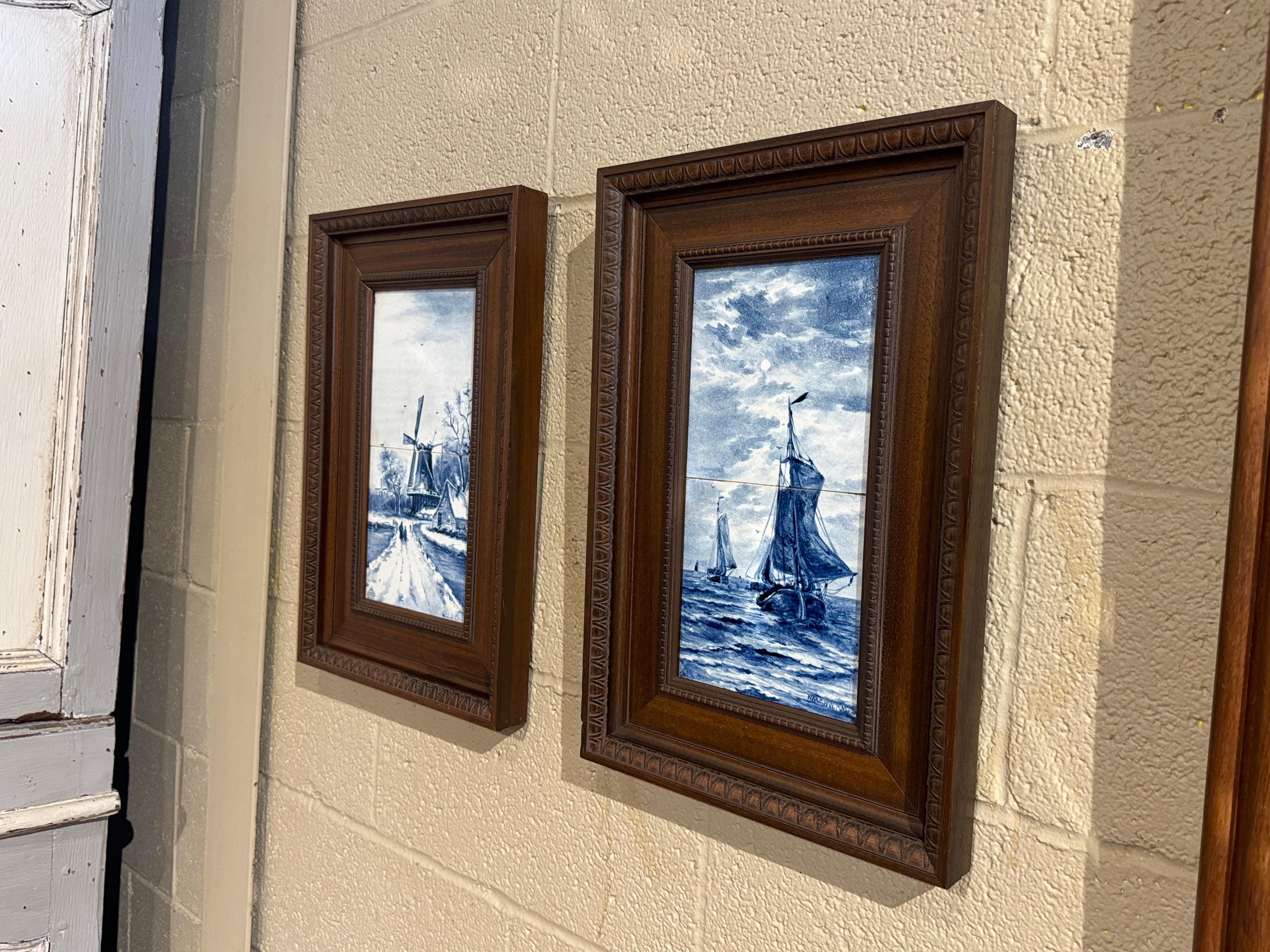 Decorate a wall with this elegant pair of antique framed Delft faience tiles! Created in France, circa 1920, each wall decor is set inside a carved walnut frame, and showcase quintessential hand painted Dutch scenes. One artwork depicts a classic