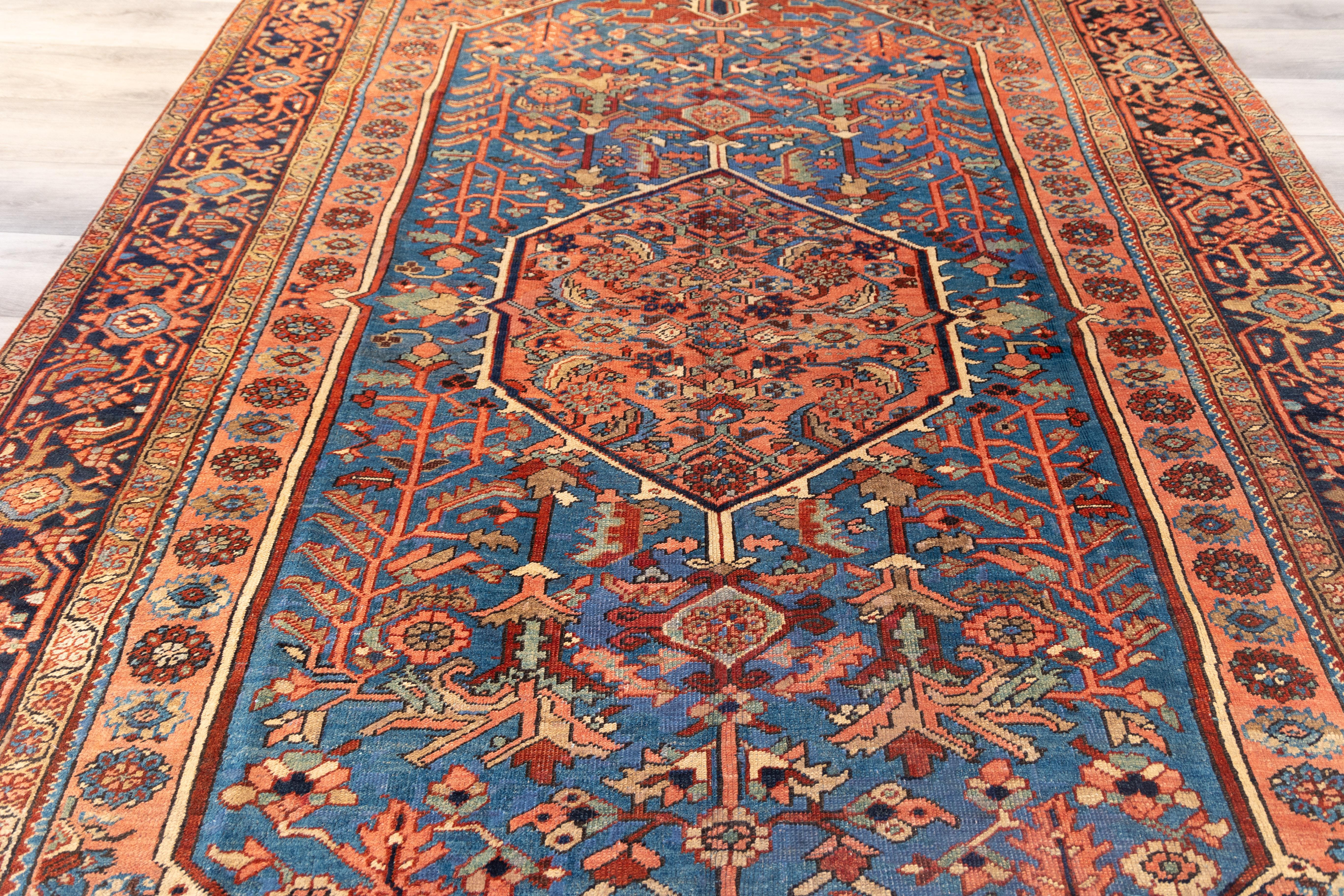  early 20th-century Heriz rug with a  striking central medallion in coral red, set within a field of deep cerulean blue teeming with angular vinery, palmettes, and stylized blossoms. The stepped corners echo the medallion in color and motif, while
