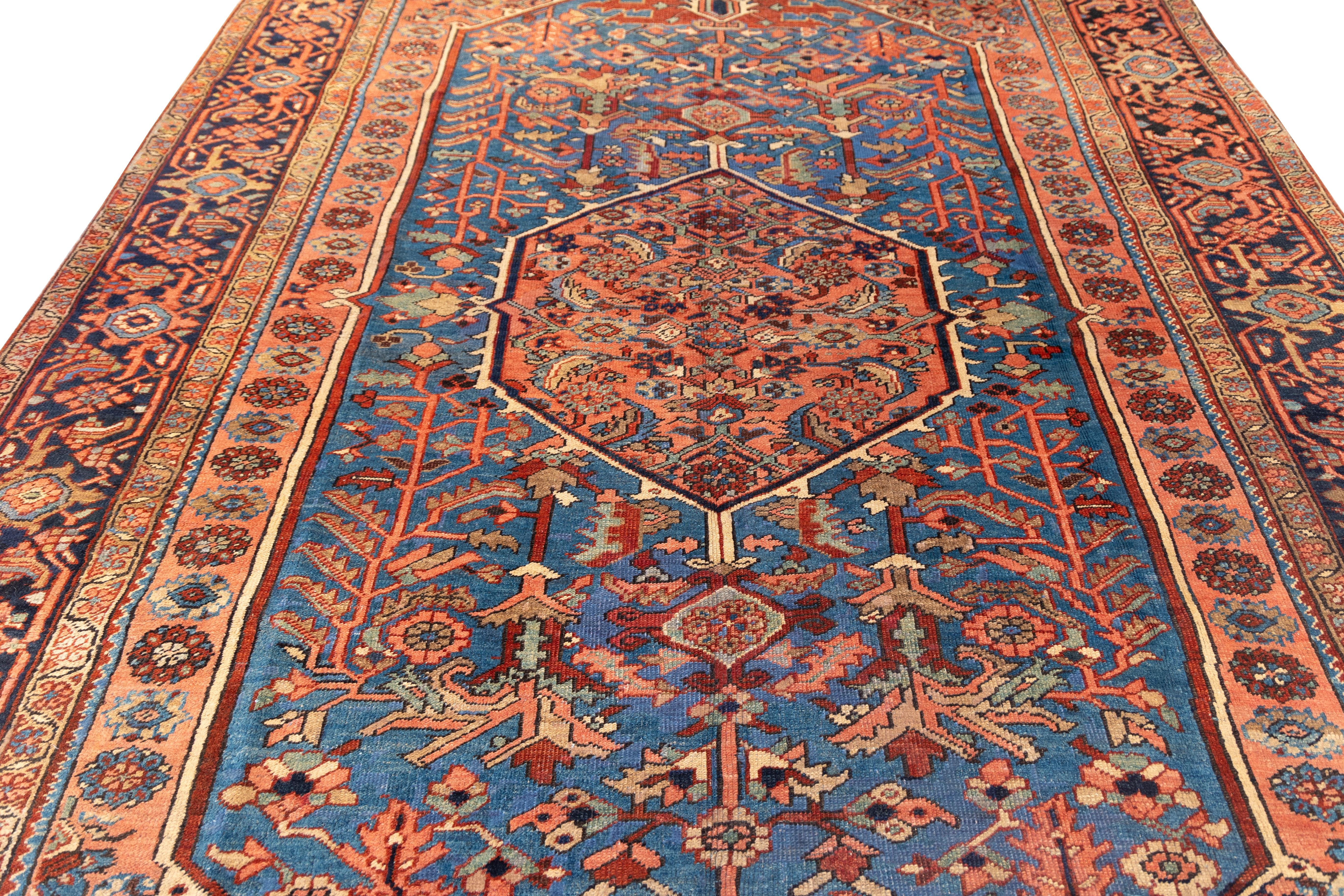  early 20th-century Heriz rug with a  striking central medallion in coral red, set within a field of deep cerulean blue teeming with angular vinery, palmettes, and stylized blossoms. The stepped corners echo the medallion in color and motif, while