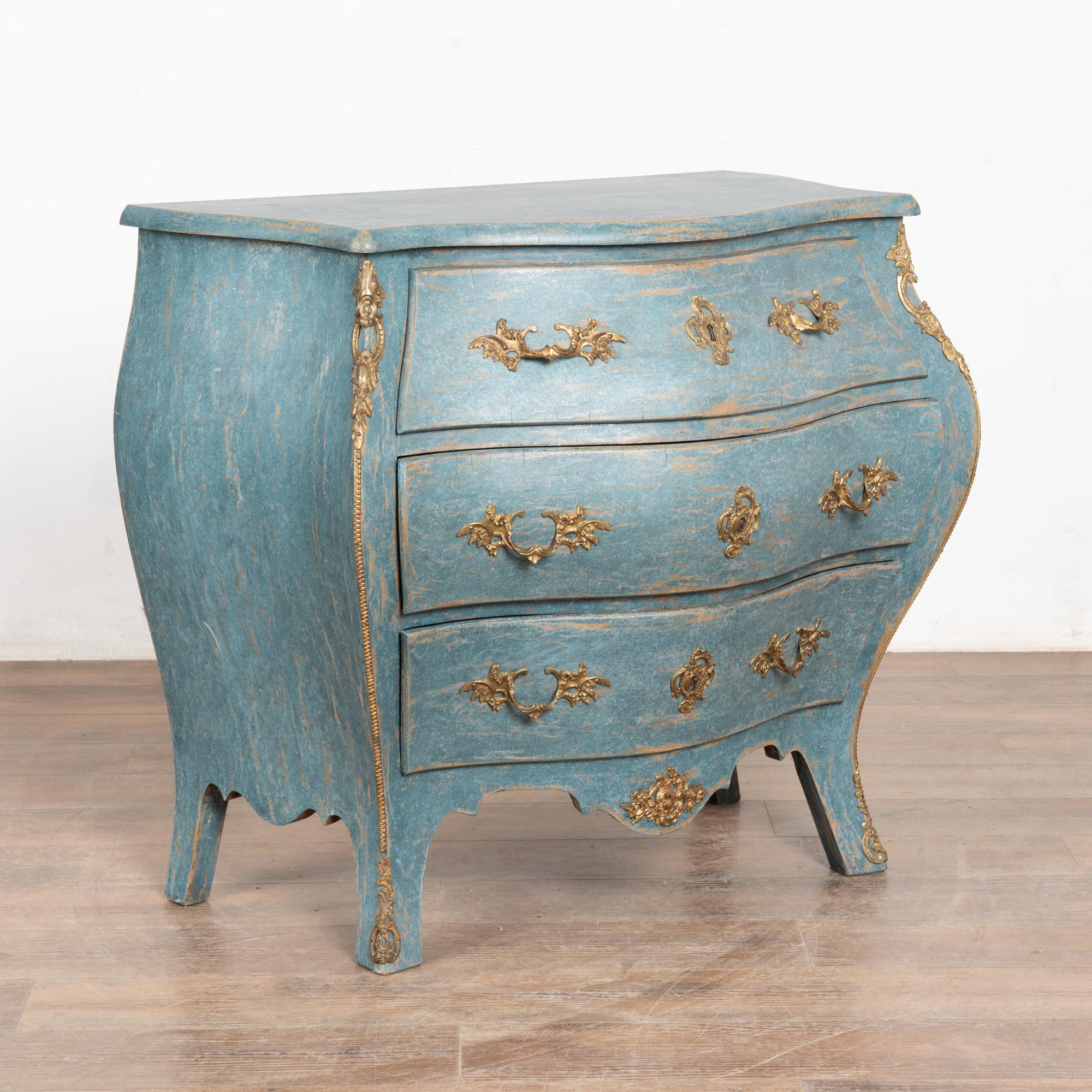 It is the bombay curves accented with brass ormolu and saber feet turning gently outwards that draws one to this striking small chest of three drawers.
Later professionally painted in layered shades of blue and lightly distressed to fit the age and