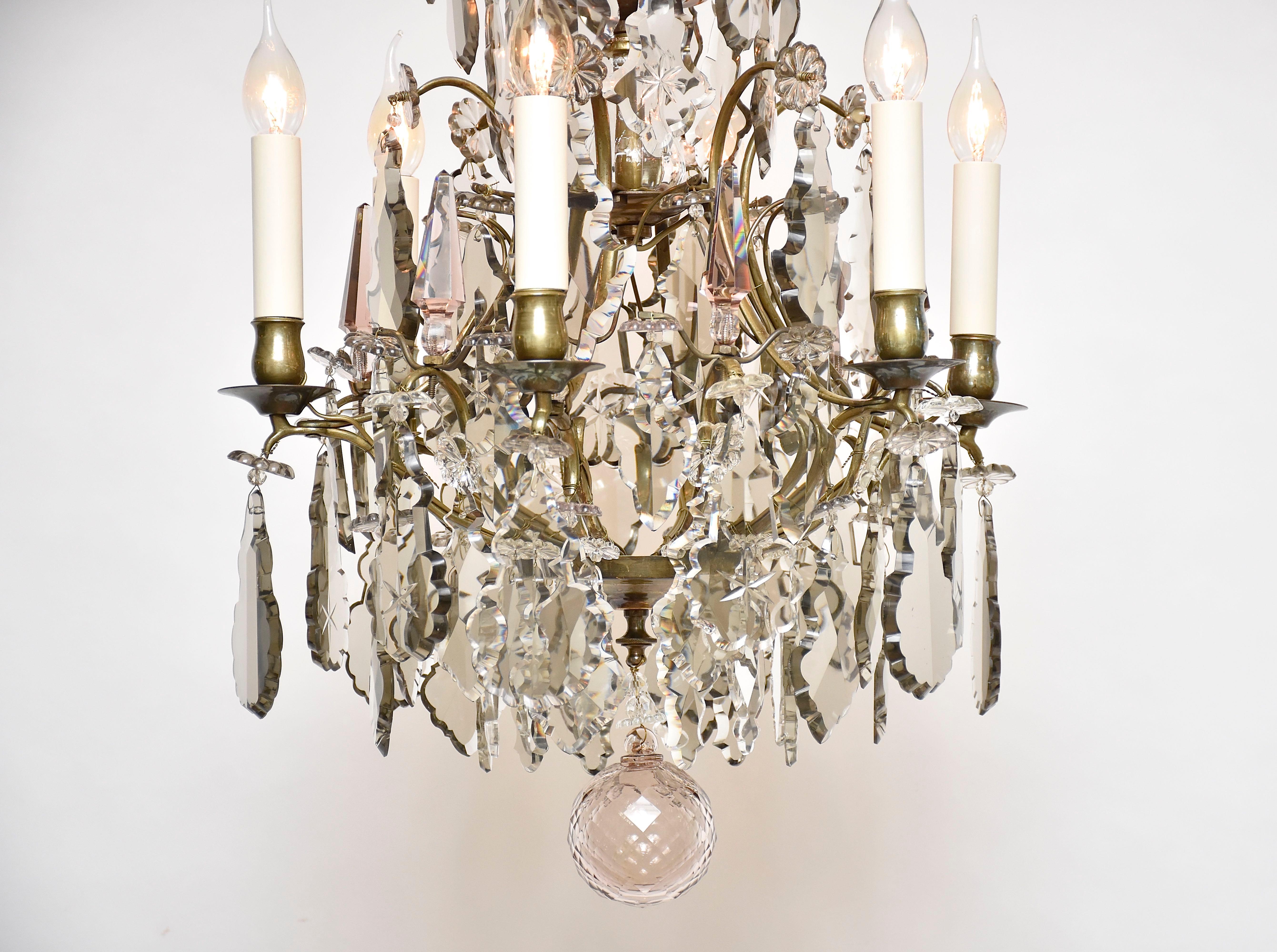 An elegant Rococo style brass and crystal chandelier.
With 6 lights.
With an old gold patina. Decorated with several large clear and soft coloured cut crystal pendeloques, large flower rosettes and poignards. 
The arms of the crown are connected