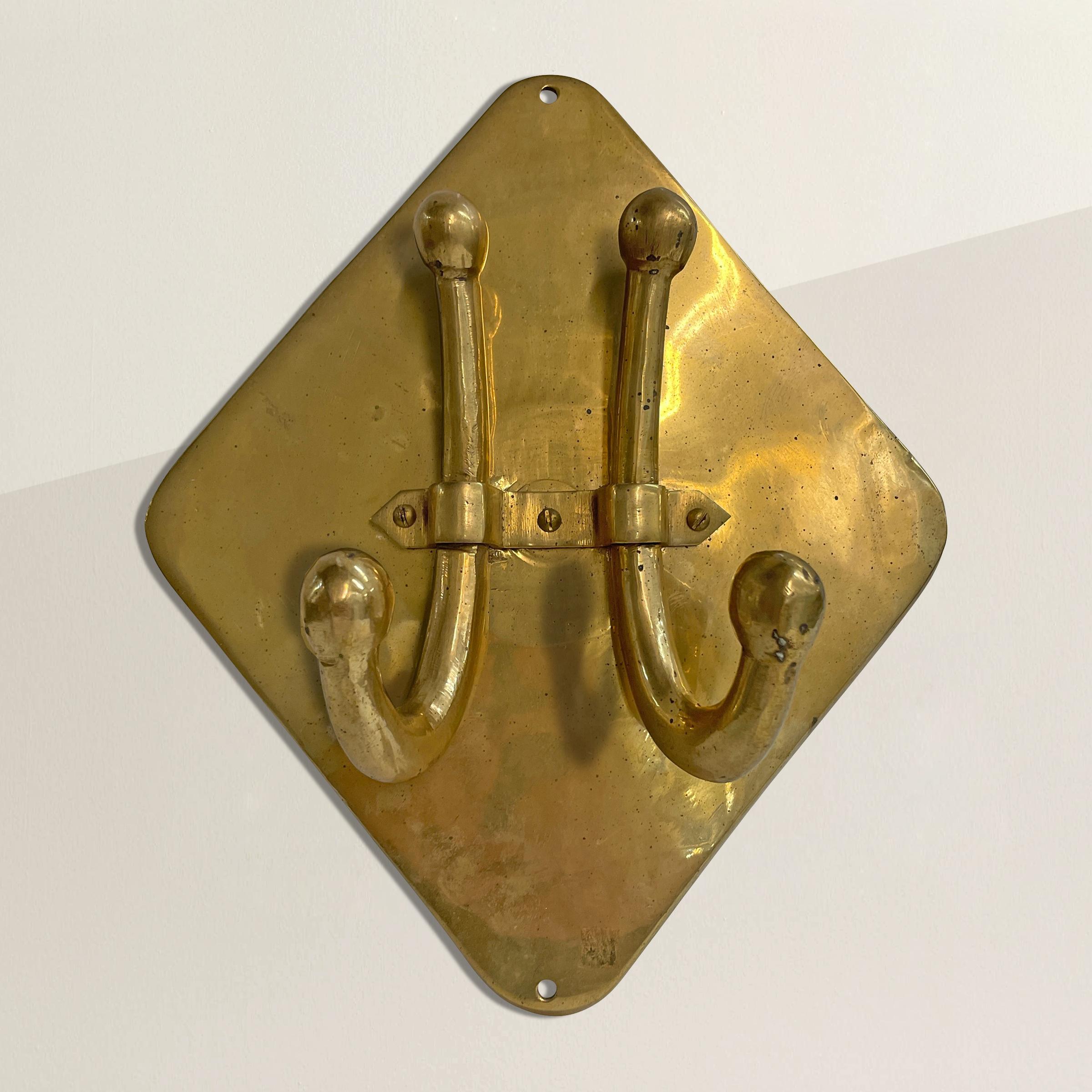 A beautiful early 20th century English brass wall-mounted coat and hat hook with two large hooks mounted to a diamond wall plate.