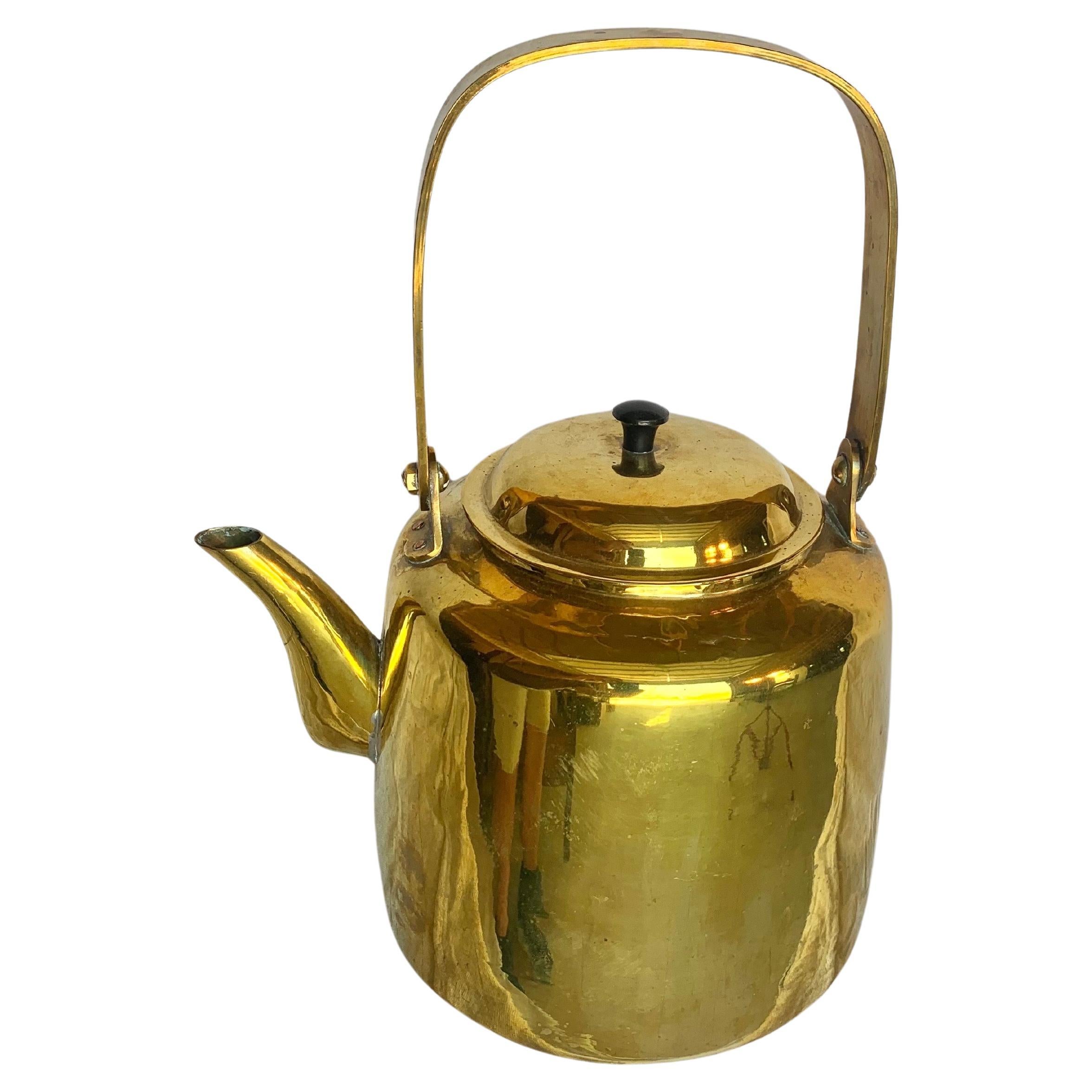 Cette bouilloire du début du XXe siècle a été fabriquée en laiton par des artisans au début des années 1900. La pièce comporte une poignée détaillée qui mène à une bouilloire surdimensionnée. Les coutures sont toutes soudées à la main et le design a