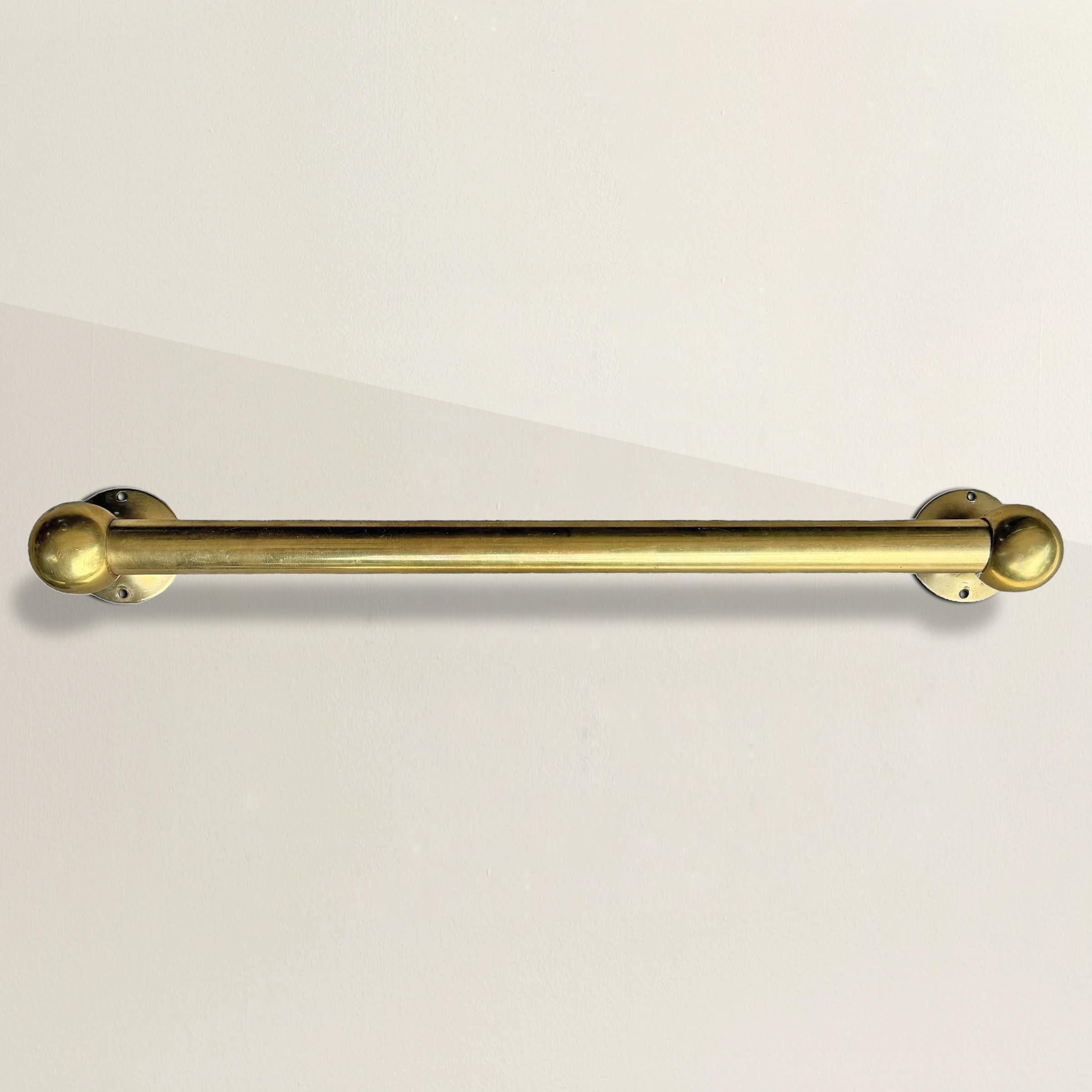 This early 20th-century American brass towel bar showcases timeless design and durability. The wide gauge bar is securely held by elegant spherical ball ends, providing both functionality and a refined aesthetic. Finished in unlacquered brass, it