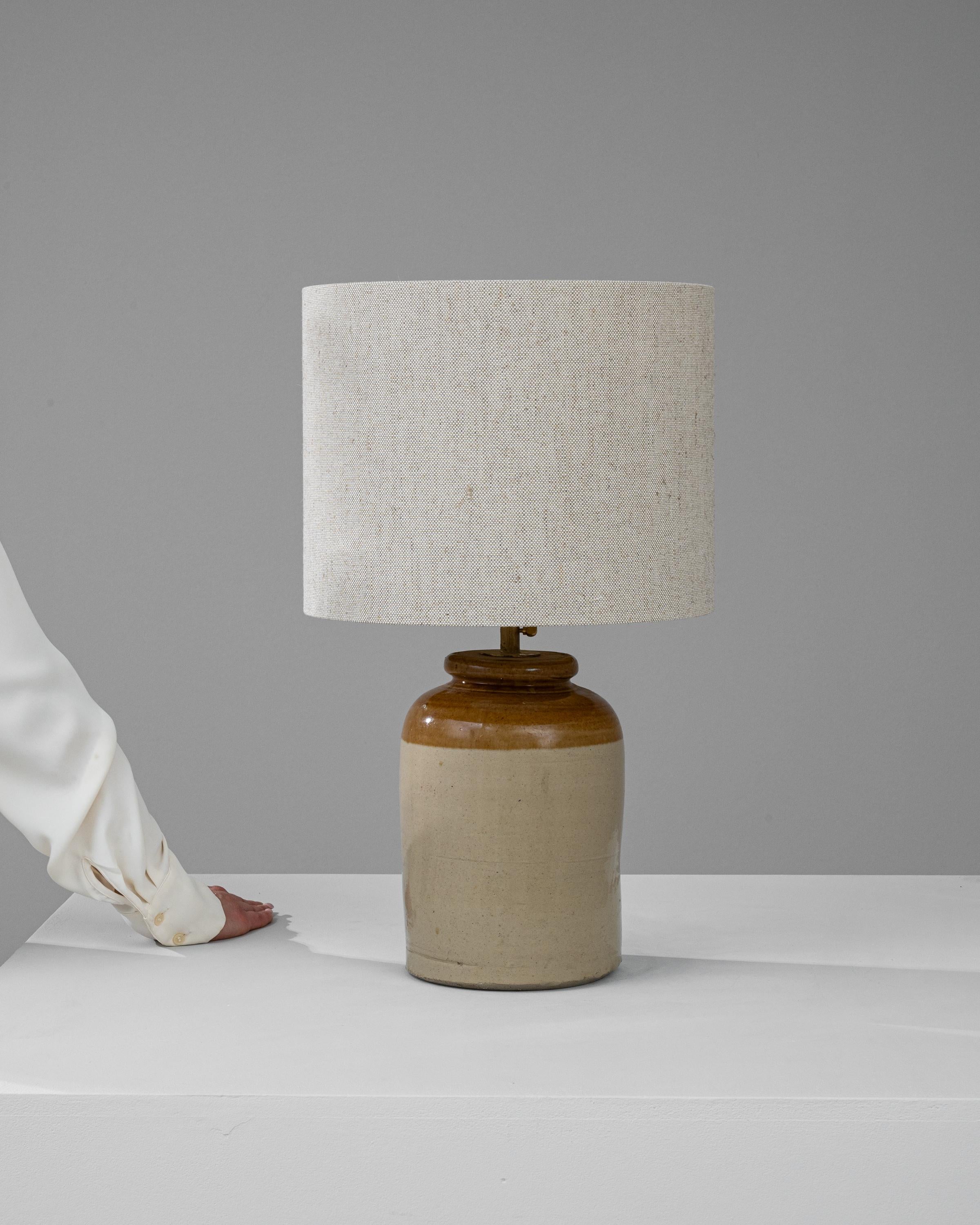 This Early 20th Century British Ceramic Table Lamp marries the unadorned grace of rustic pottery with the understated elegance of modern design. Its stout ceramic base, displaying a pleasing contrast between the natural beige body and the rich,