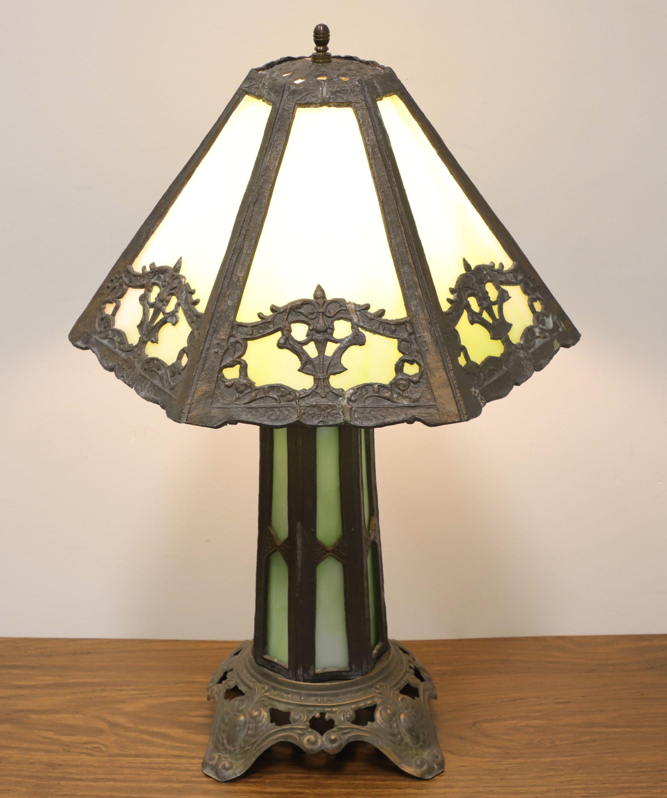 An antique Art Deco style slag glass table lamp, unbranded. Slender six-sided bronze body with green/white color slag glass inserts, decorative bronze base with four feet, and a decorative bronze hexagon shaped shade with green/white color slag