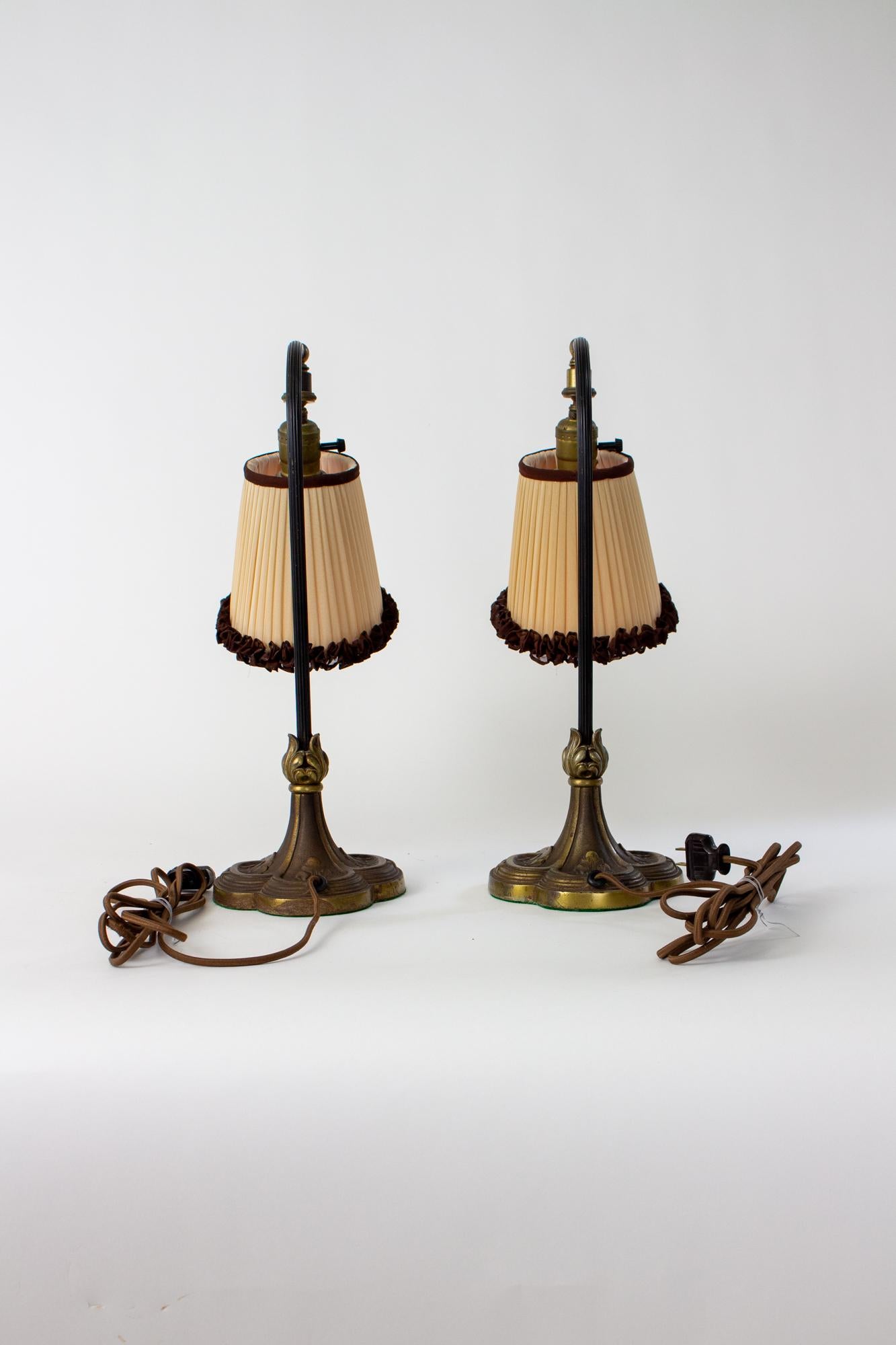 Early 20th Century bronze curved neck table lamps with original silk shades. A pair of table lamps ideal for a desk or bedside table. Club shaped bases with neoclassical elements, made of cast bronze. Curved reeded stem with an articulating swivel