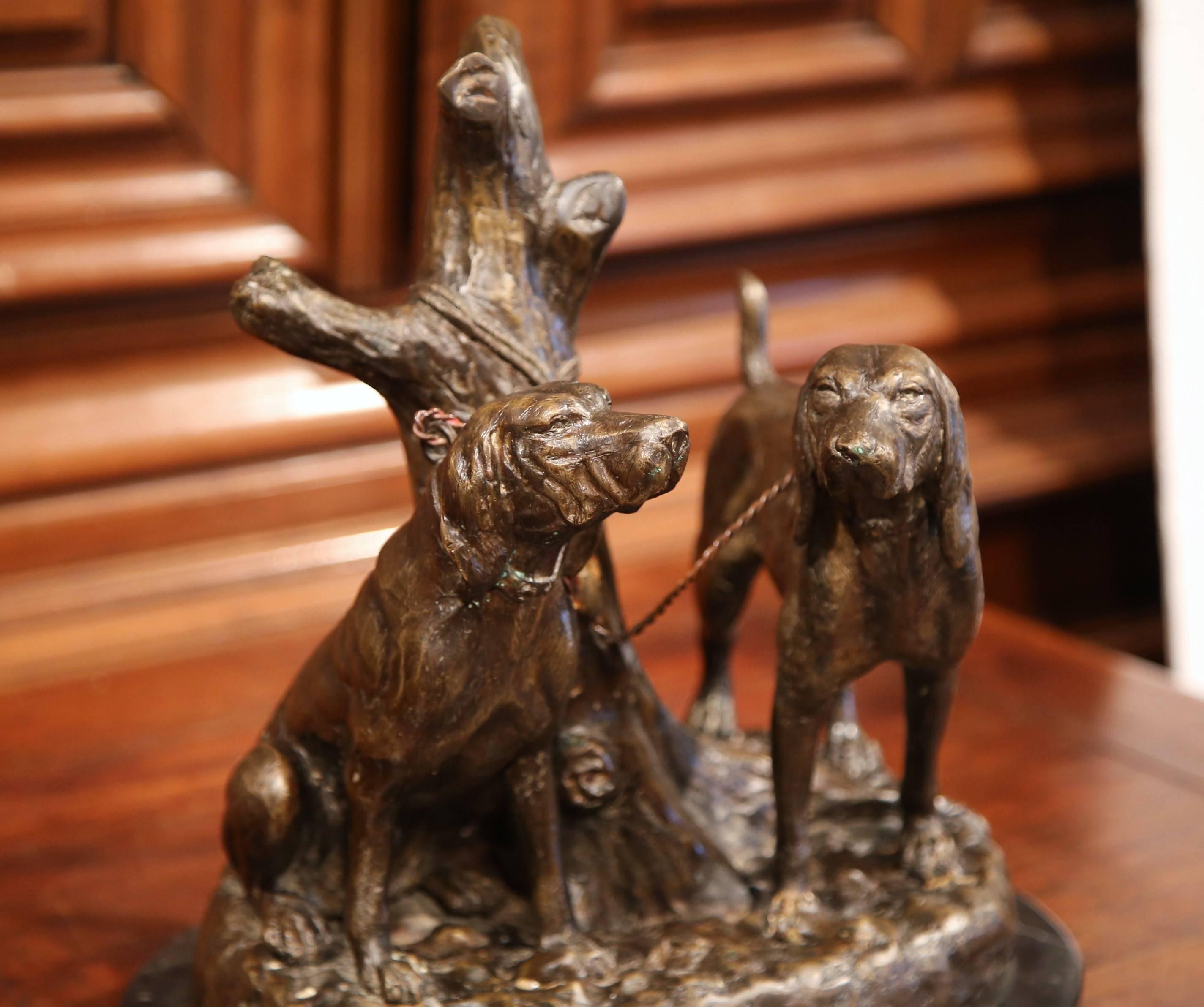 This beautiful, antique bronze composition was crafted in France, circa 1920. The traditional animal sculpture features two hunting dogs chained up together to a tree trunk. The hounds sit on a sturdy, black oval marble base, and the canine figure