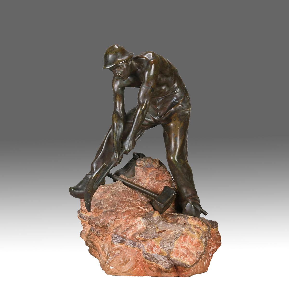  A very fine early 20th Century bronze figure of a miner using a pickaxe to dig his way through a large boulder with his satchel and other tools layed out on the ground. The bronze exhibiting excellent hand finished surface detail and good rich