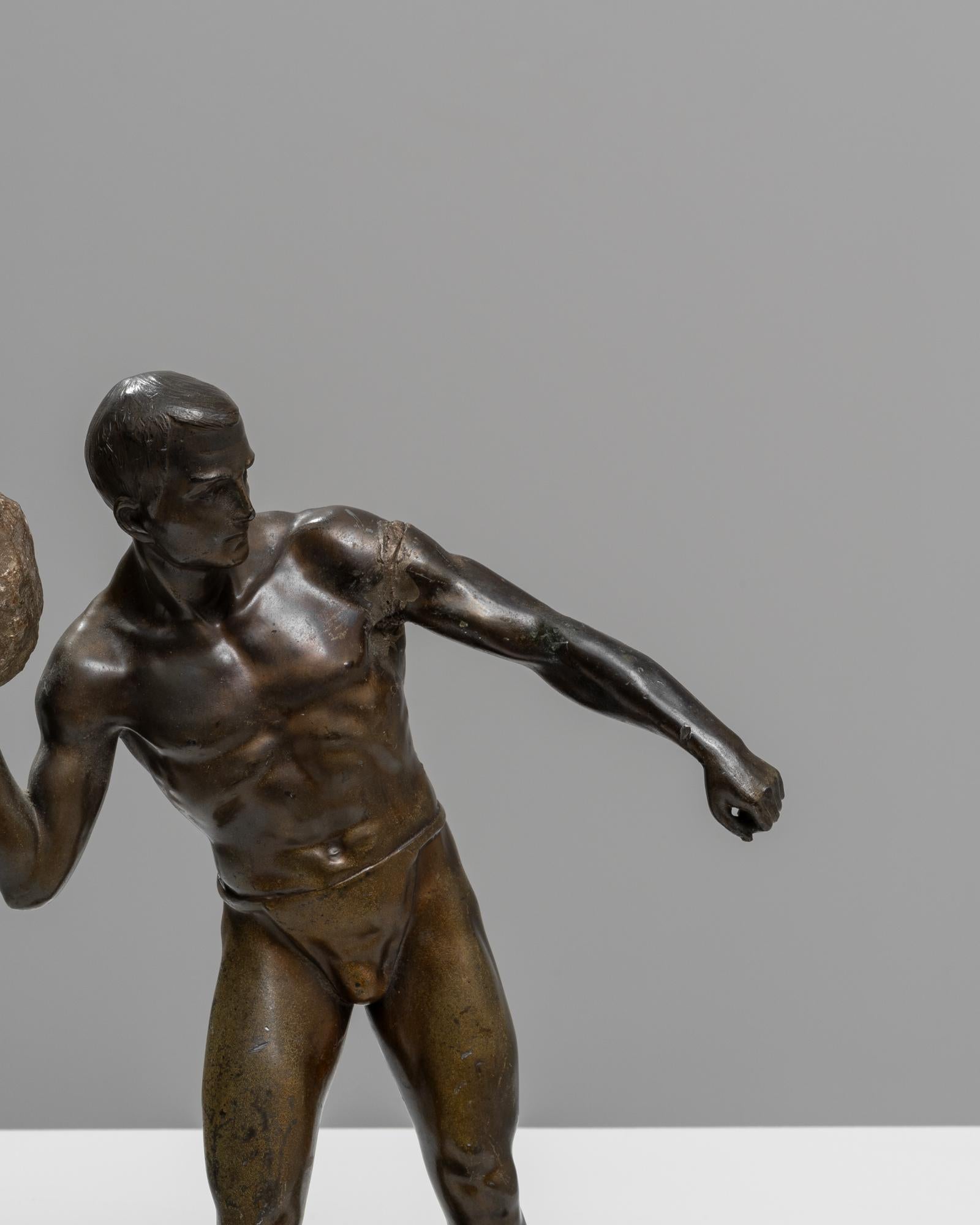 Showcase a piece of dynamic artistry in your space with this early 20th-century bronze sculpture. This striking figure captures a moment of intense action, depicting a muscular male form in mid-throw, wielding a stone with remarkable force and