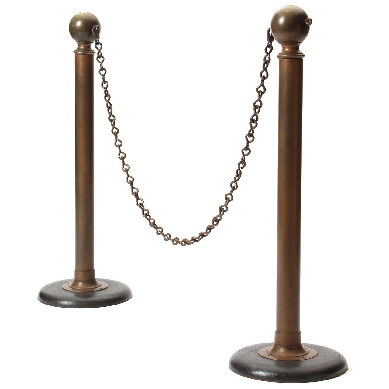 A pair of bronze standing security poles with an attached chain on cast iron bases. (Chain max. length: 51