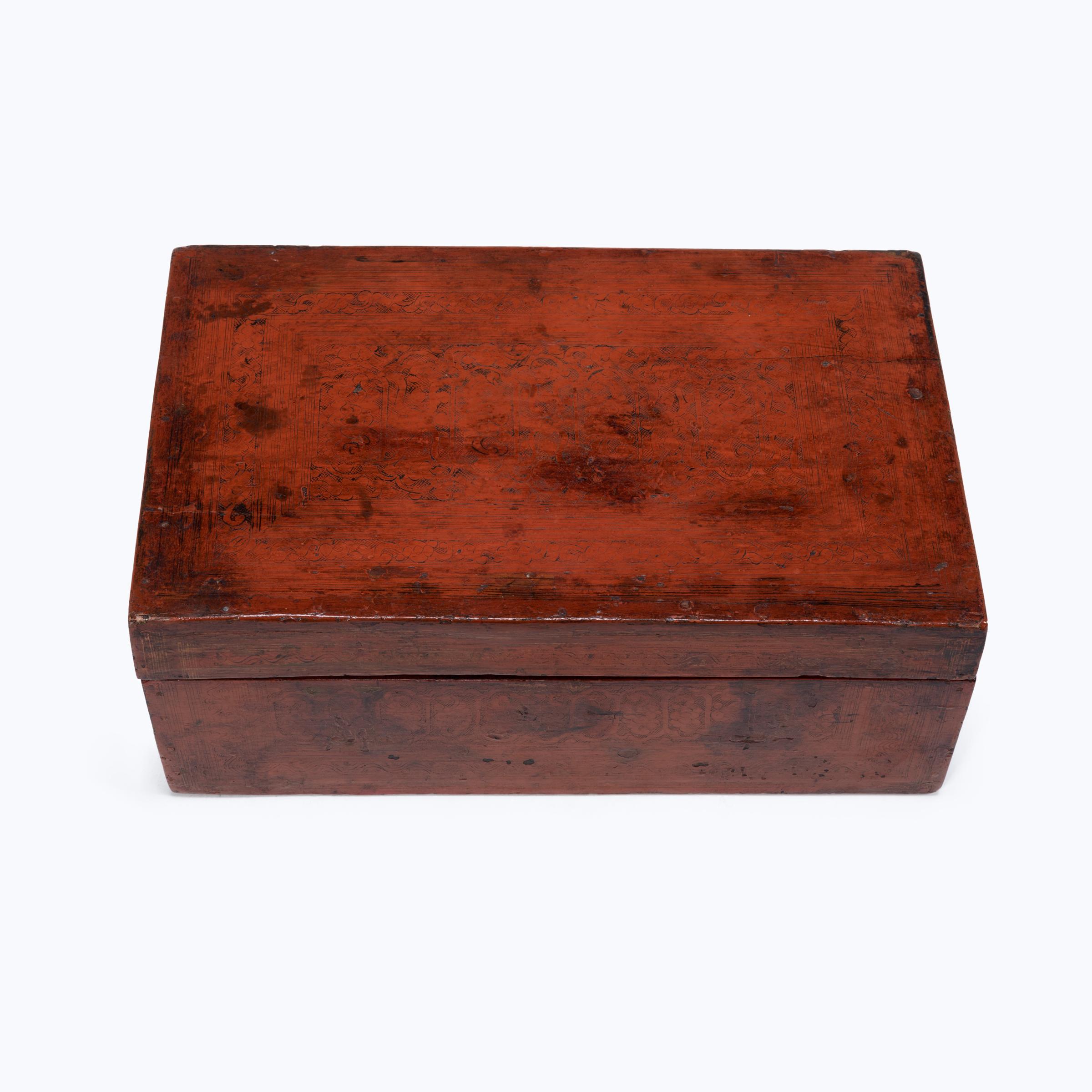 Crafted in early 20th century Burma, this rectangular box is cloaked in layer upon layer of brilliant red-orange cinnabar lacquer. Decorated in a style known as 