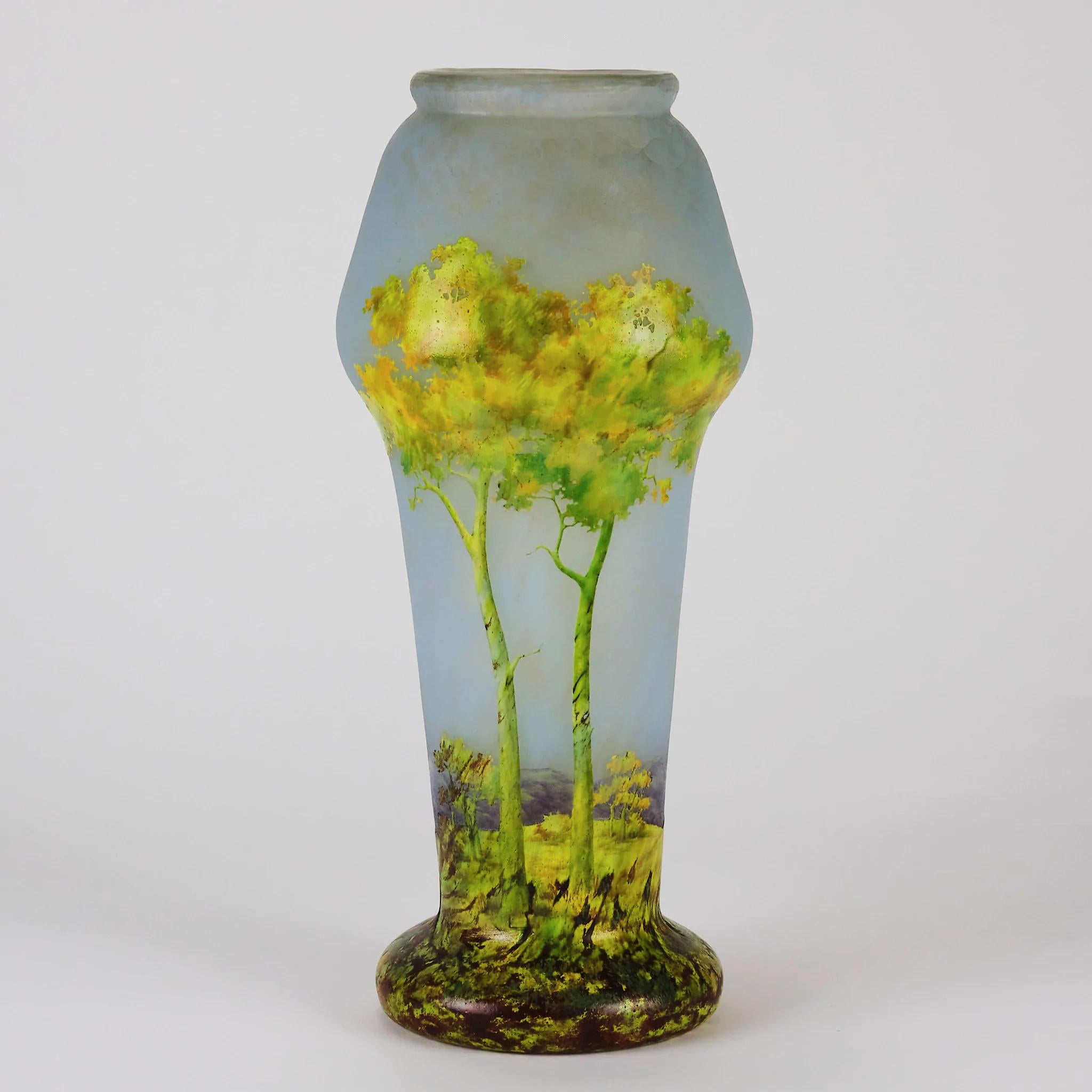 A stunning vibrant cameo glass vase etched and enamelled with brightly colored trees in the foreground against a hilly background and deep sky blue horizon, exhibiting excellent color and detail, signed Daum Nancy and initialled SH for in-house