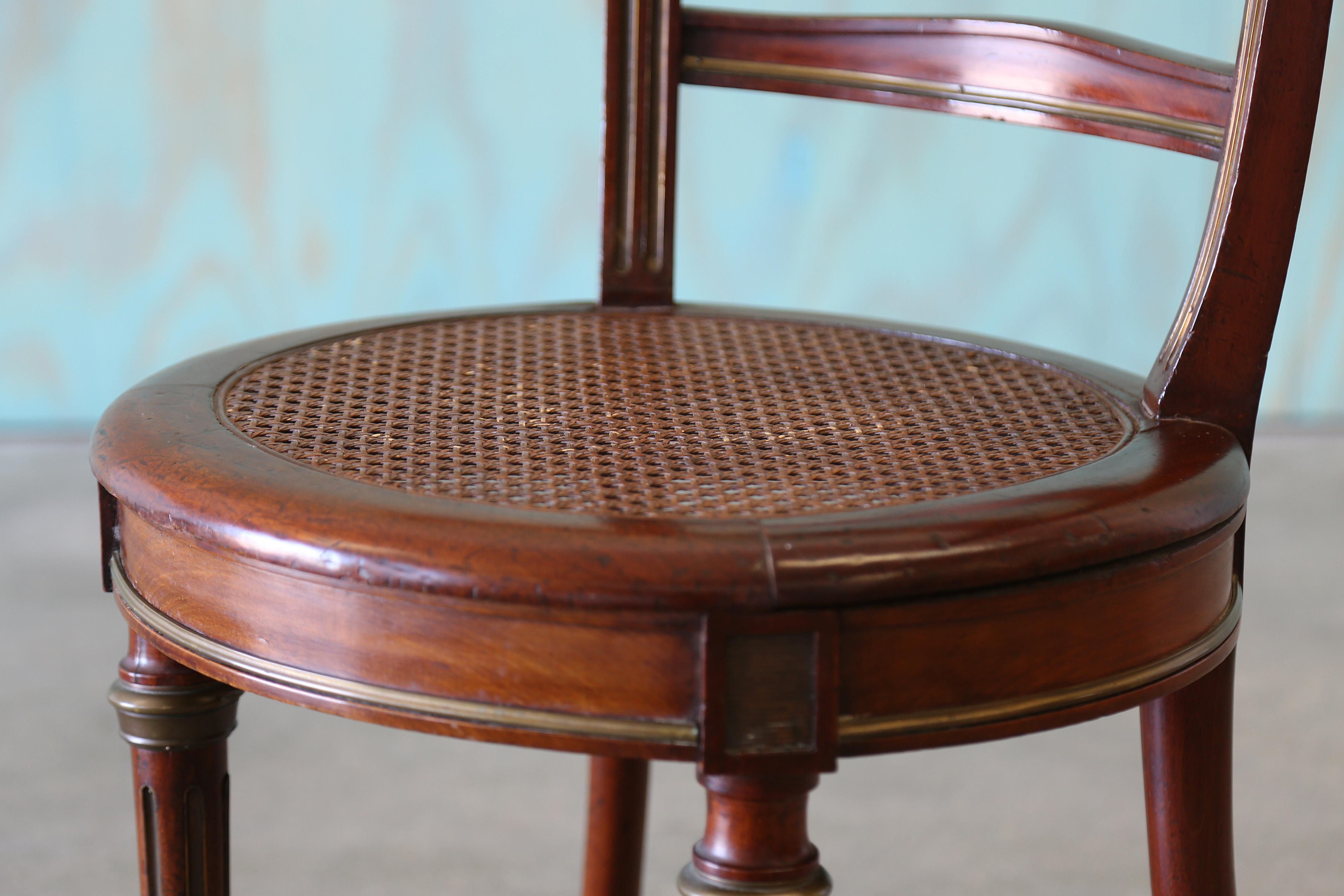 Early 20th century cane seat cockfighting / tub / captains chair Louis XVI style . Frame appears to be mahogany and features a round, caned seat. Legs are reeded, and tapered with brass detailing. Unknown maker.

Unsigned.

Dimensions: 30.5” High