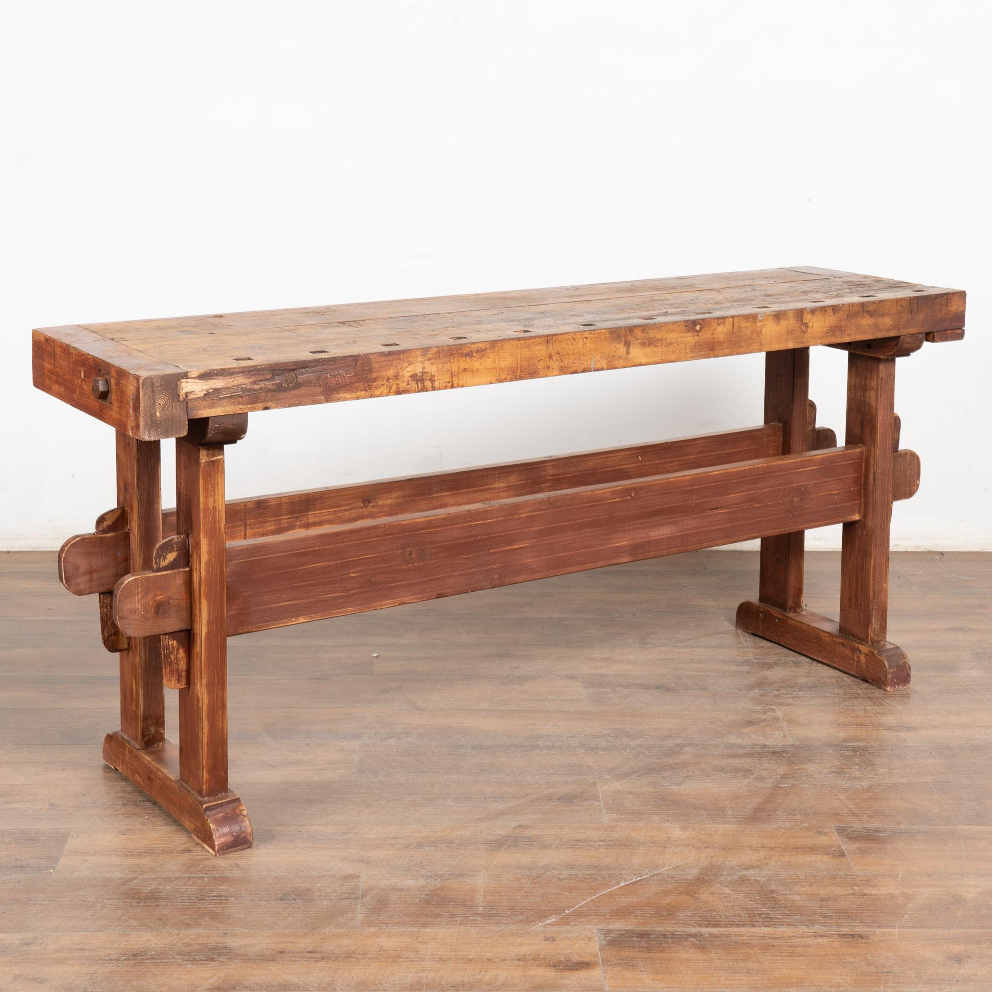 The worn patina of this carpenter's workbench is a reflection of its age and years of use. Every ding, scratch, gouge, and stain enrich the character and appeal of this old work table which still maintains the original brick red/brown painted finish