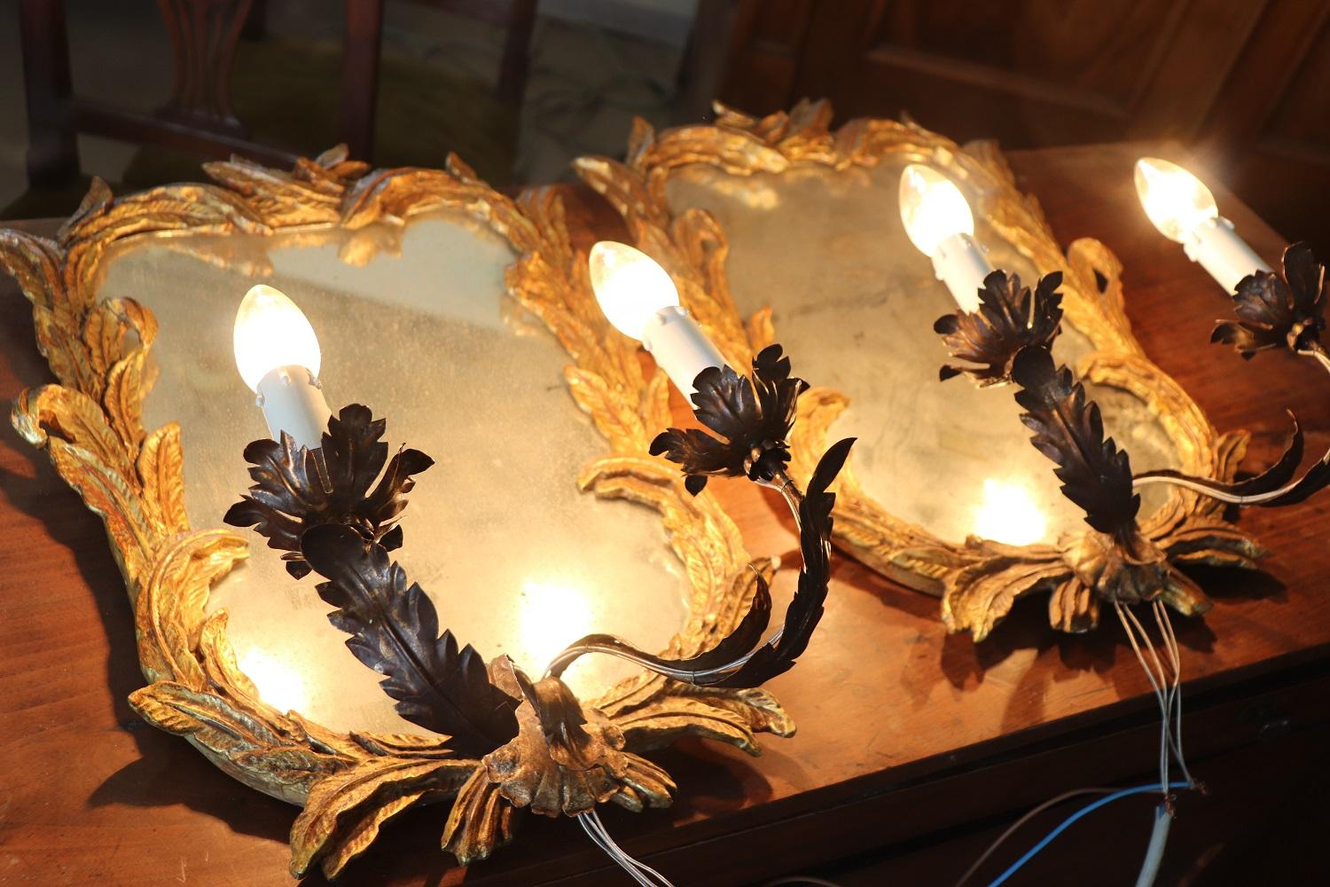 Lovely pair of sconces with mirror in carved and gilded wood. The mirror is antique, the reflected image is damaged. Each mirror has two lights. Rewired electrical system.