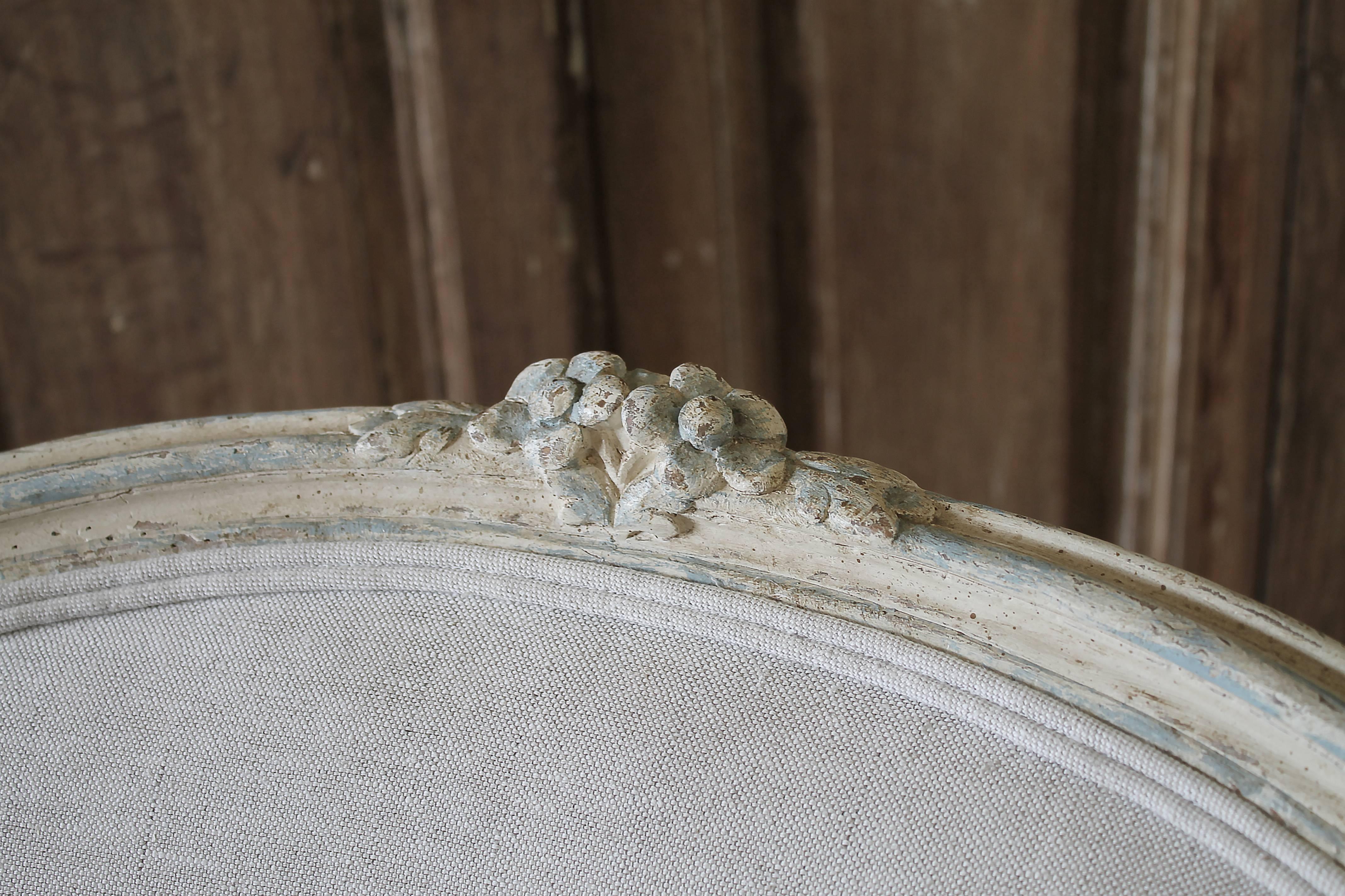 Early 20th century carved and painted bergere chair upholstered in natural linen
Original as found the painted bergere chair has a lovely patina painted finish in an off-white, almost creamy greige color, with pale blue painted tones peeking