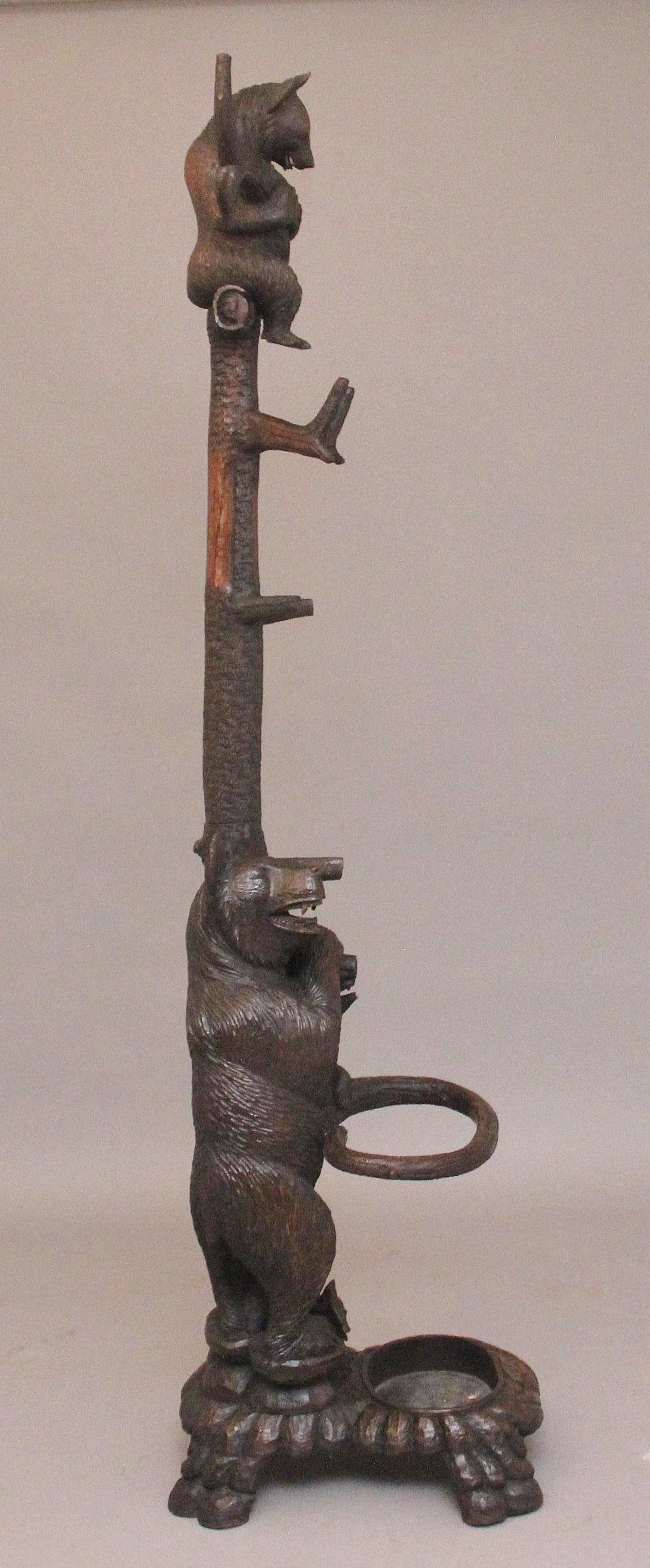 A finely carved early 20th Century walnut black forest bear hall stand with a cub playing in the branches above, the bear below with another cub, looking up and holding and standing on an umbrella stand, the construction is very sturdy and the