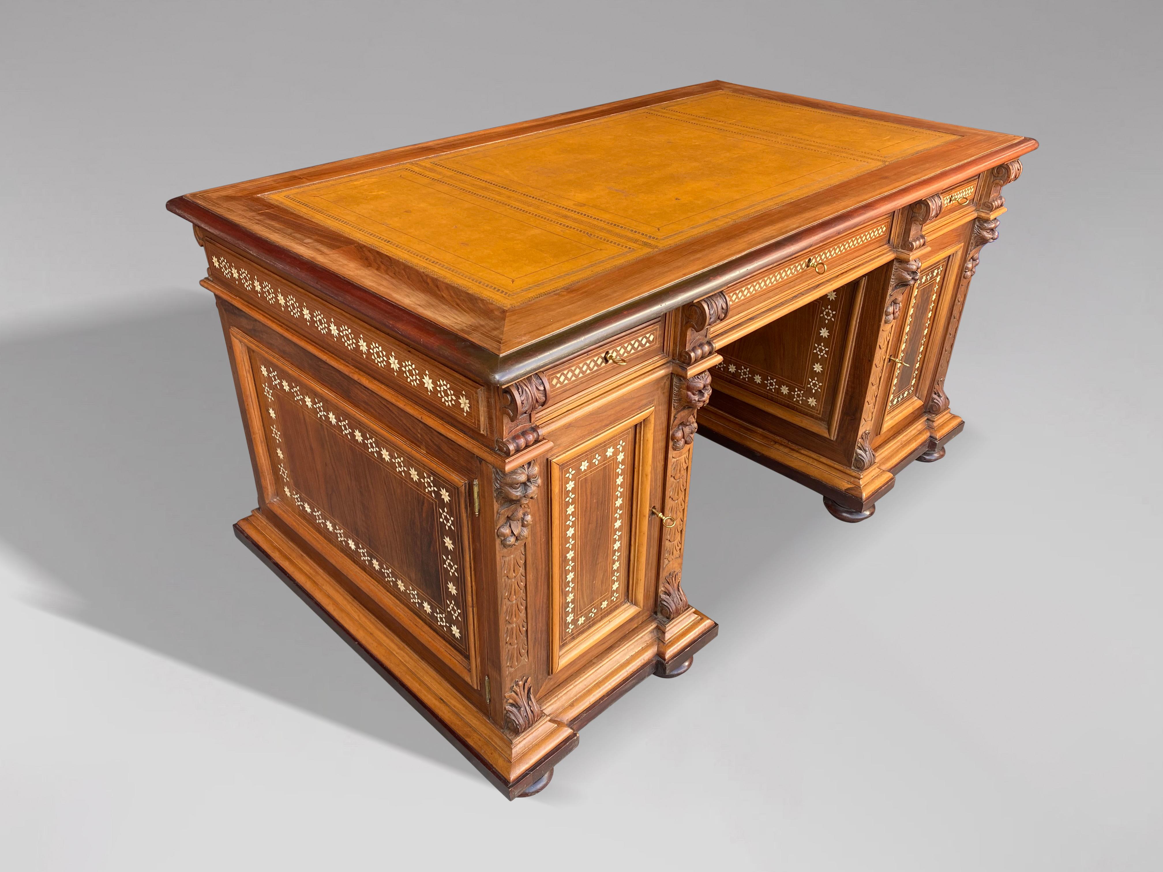 An early 20th Century walnut carved and bone inlay twin pedestal desk. With foliate geometric inlay throughout. The rectangular moulded top with yellow gilt tooled leather above an arrangement of three drawers and two pedestal cupboards, all raised