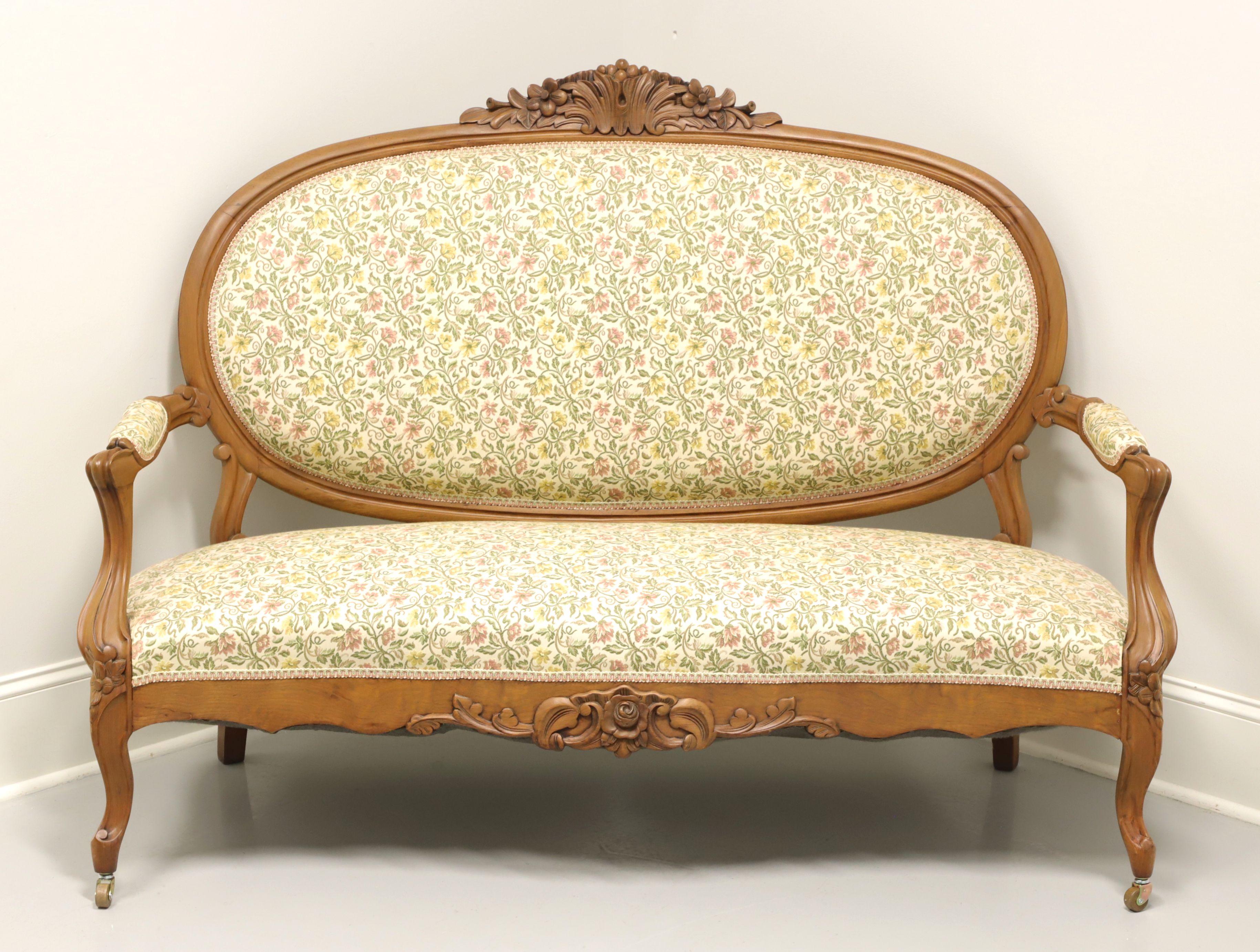 An antique French Country Louis XV style settee, unbranded. Frame made in the early 20th Century of finely carved walnut with high oval back; decorative carving to back, arms, apron & knees; fabric upholstered arms; and curved front & back legs,