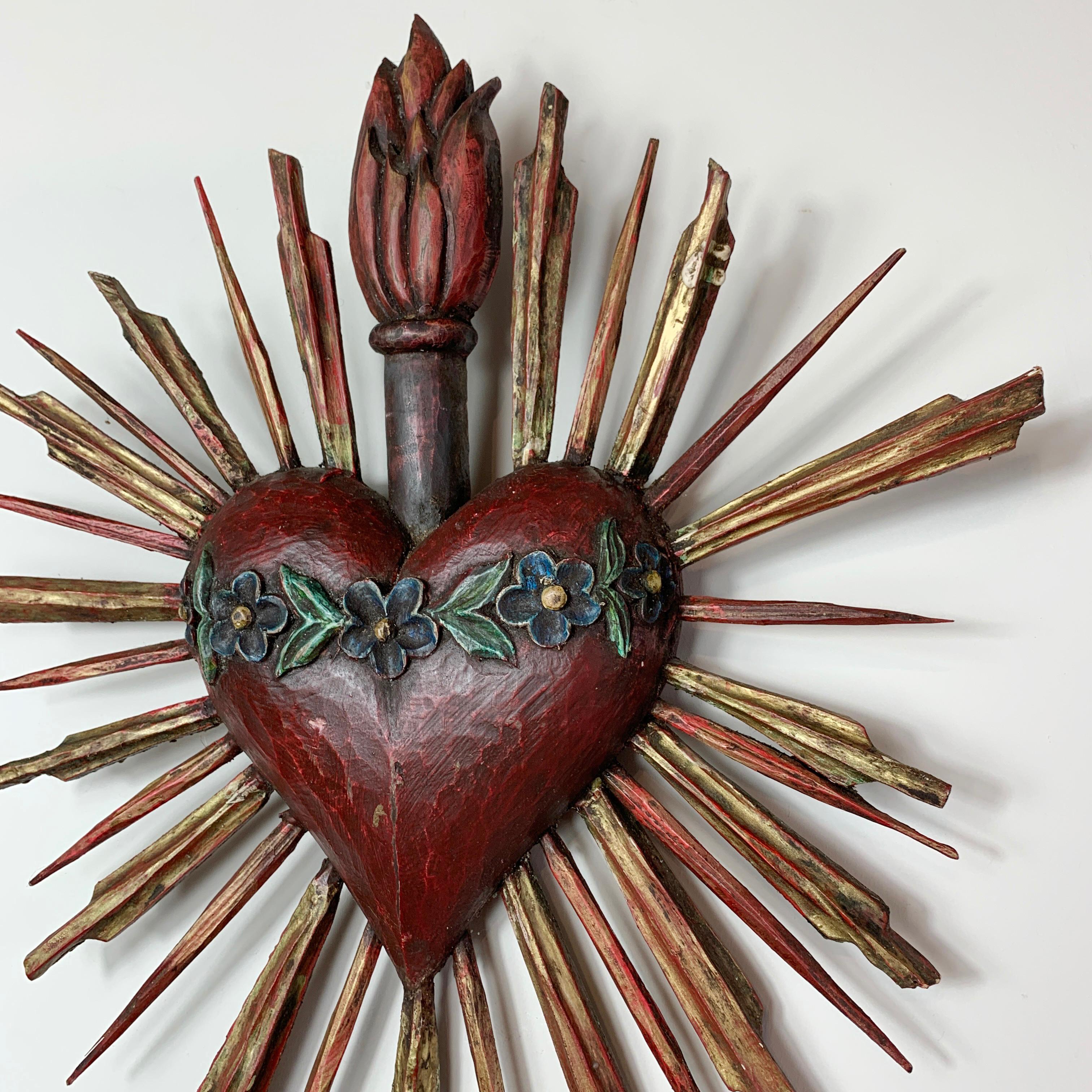 An early 20th century sacred heart carved from wood, and hand painted, it dates to around 1920 and would originally have hung in a German Church. The heart is painted with a carved floral decoration, a torchiere to the top and is surrounded by gilt