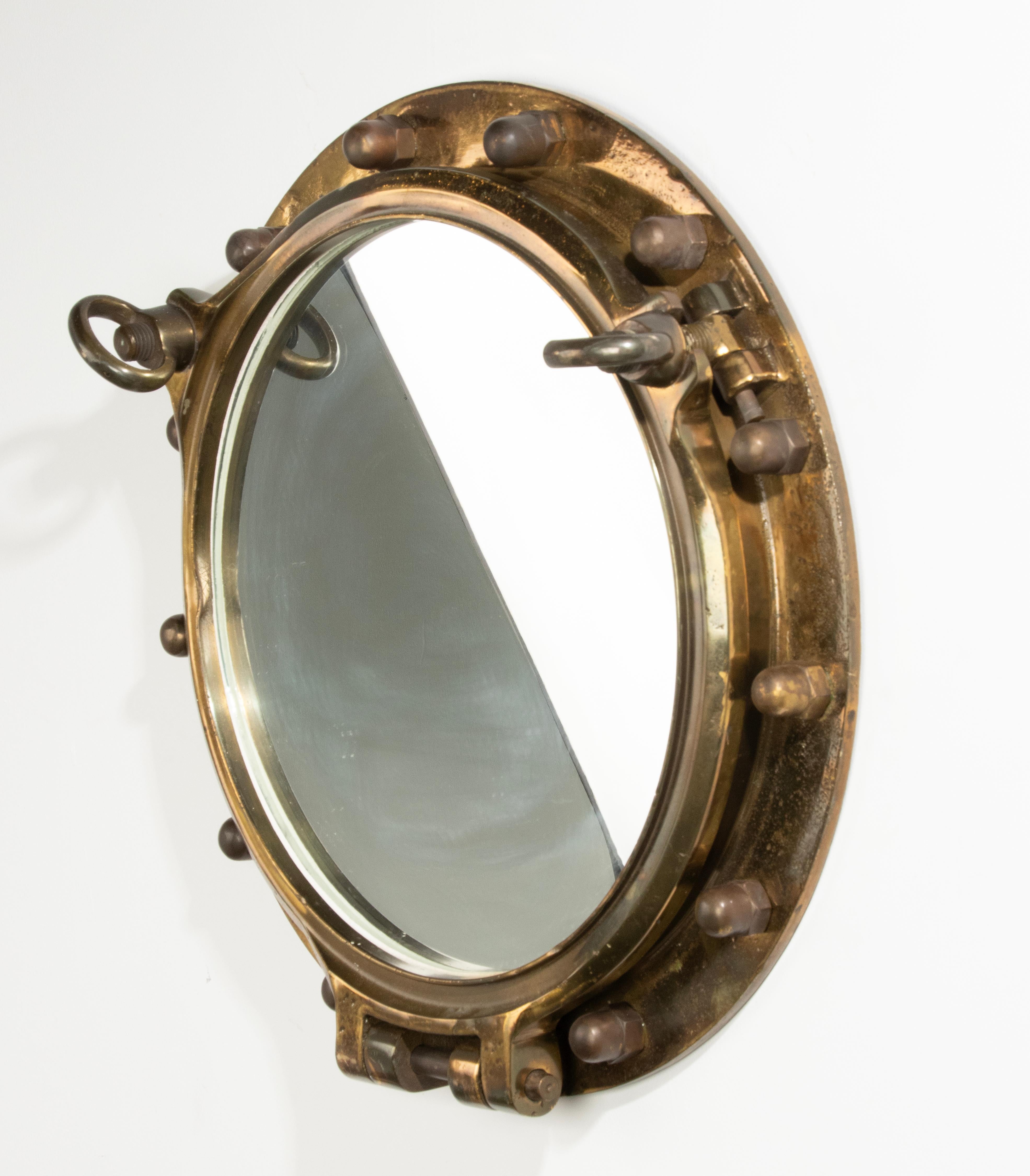 An antique heavy duty and large ship porthole wall mirror made of brass. A mirror glass has been placed inside. The whole has a beautiful old patina. The original glass is removed and replaced by a mirror glass. Some wear and small dents on the
