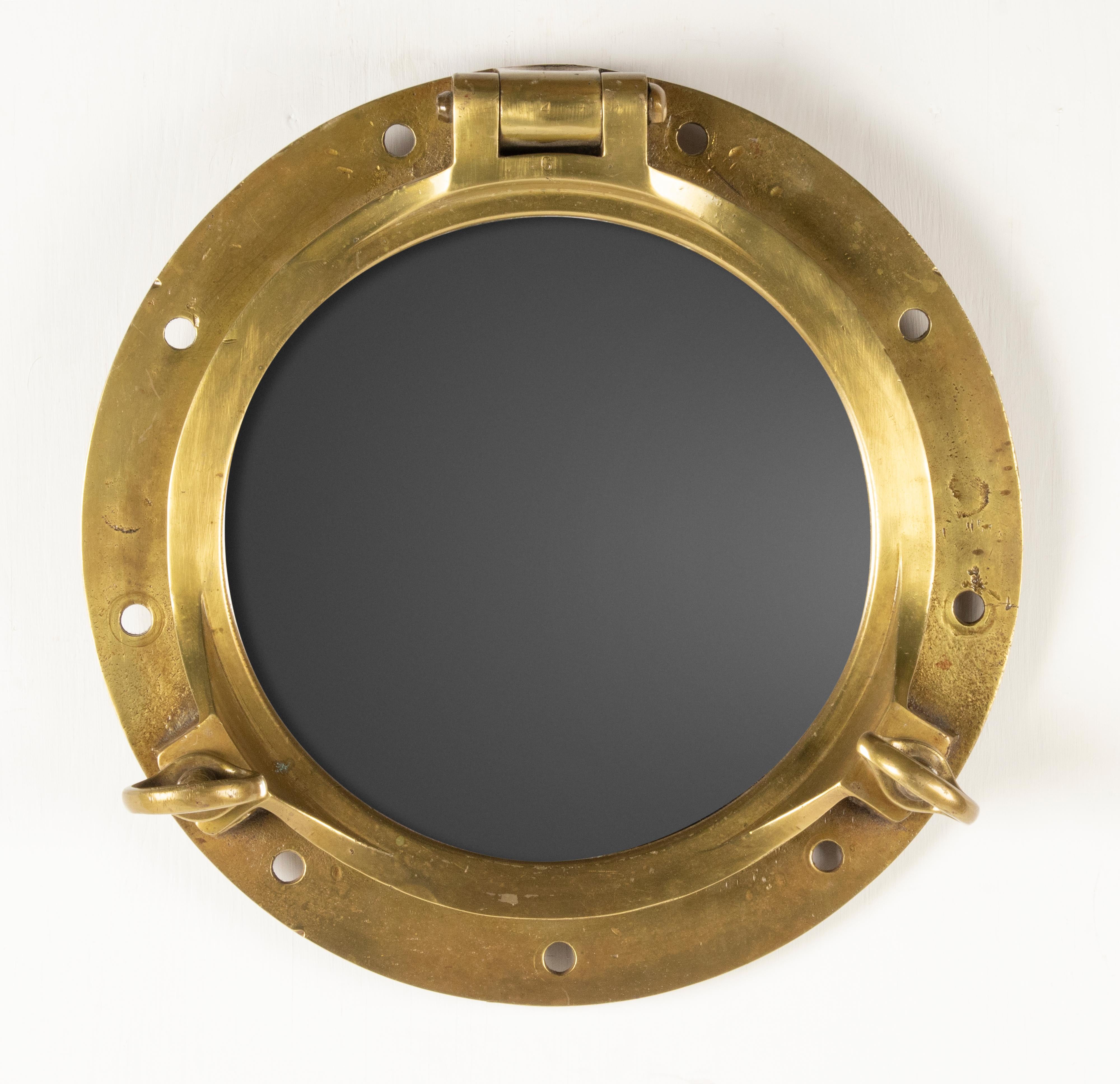 An antique heavy duty ship porthole wall mirror made of brass. A mirror glass has been placed inside. The whole has a beautiful old patina. The original glass is removed and replaced by a mirror glass, the original glass is still intact, it can be