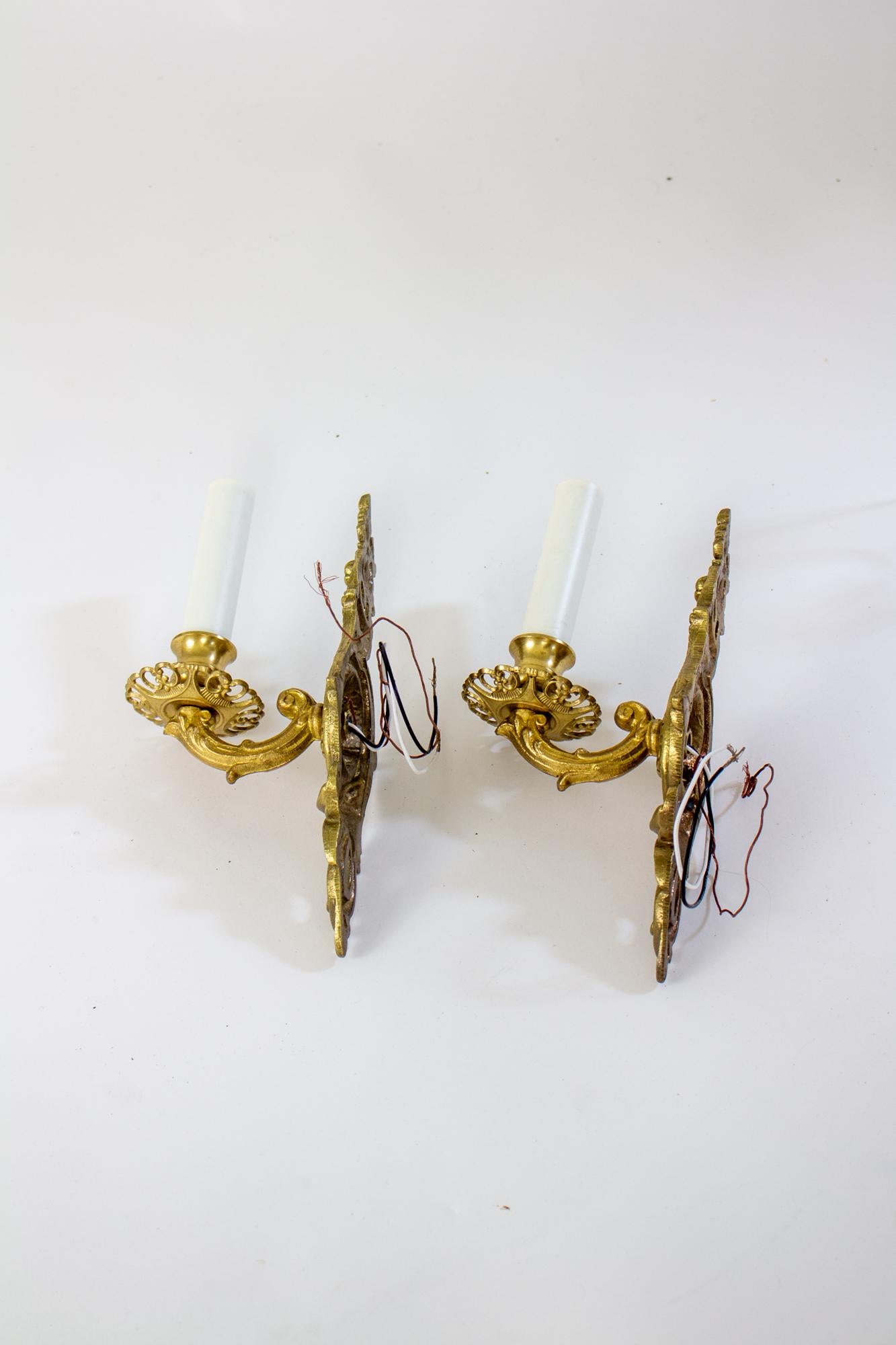 Early 20th century cast brass sconces, a pair. The backplates are from around the 1020’s, and the arms and bobeches were cast in the 1990’s, from traditional molds. The backplate is delicate and ornate, with flowers and swirled leaves. Metal in