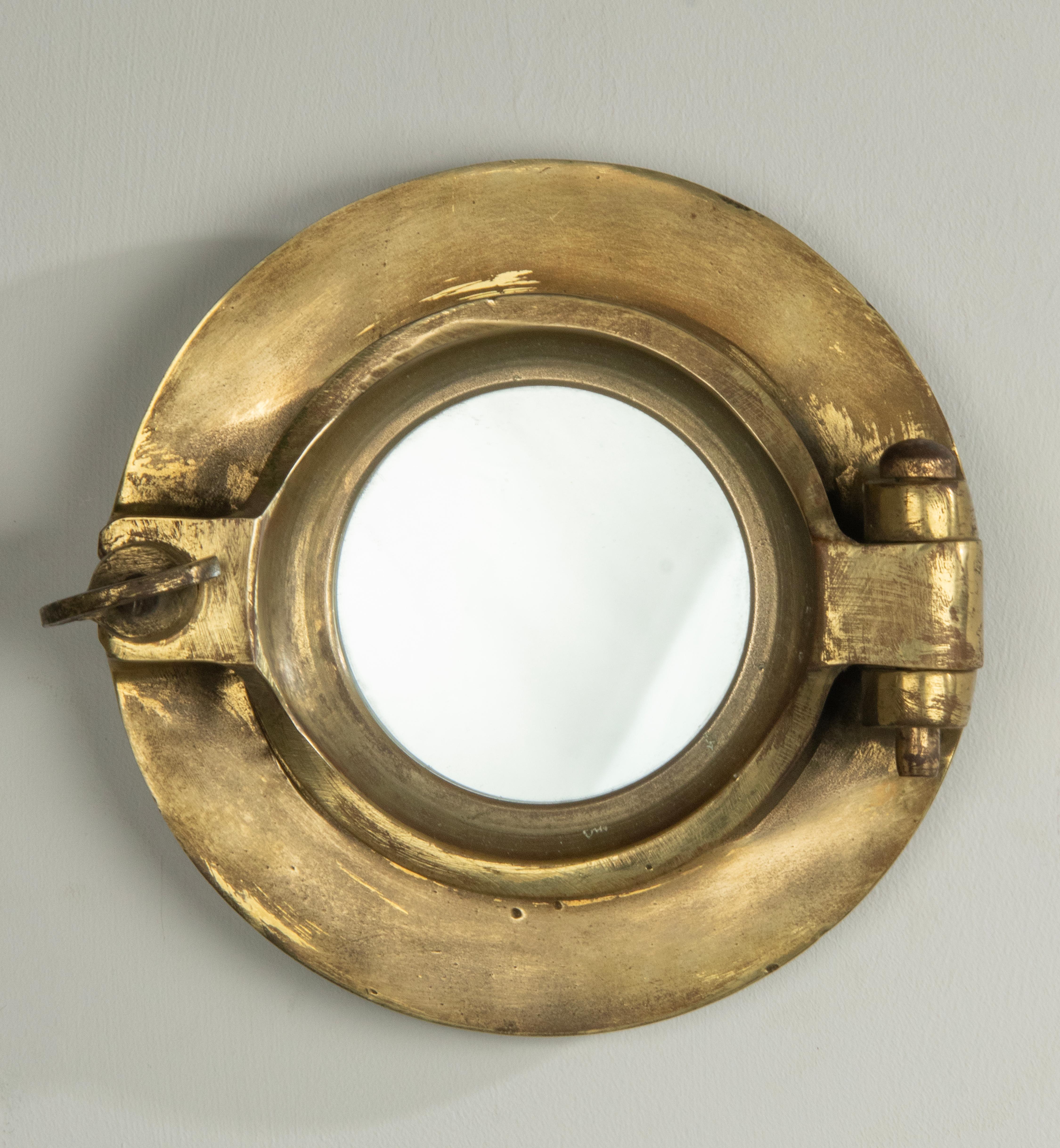 A small antique ship porthole wall mirror made of brass. A mirror glass has been placed inside. The whole has a beautiful old patina. The original glass is removed and replaced by a mirror glass. This maritime object was made around 1910-1930,