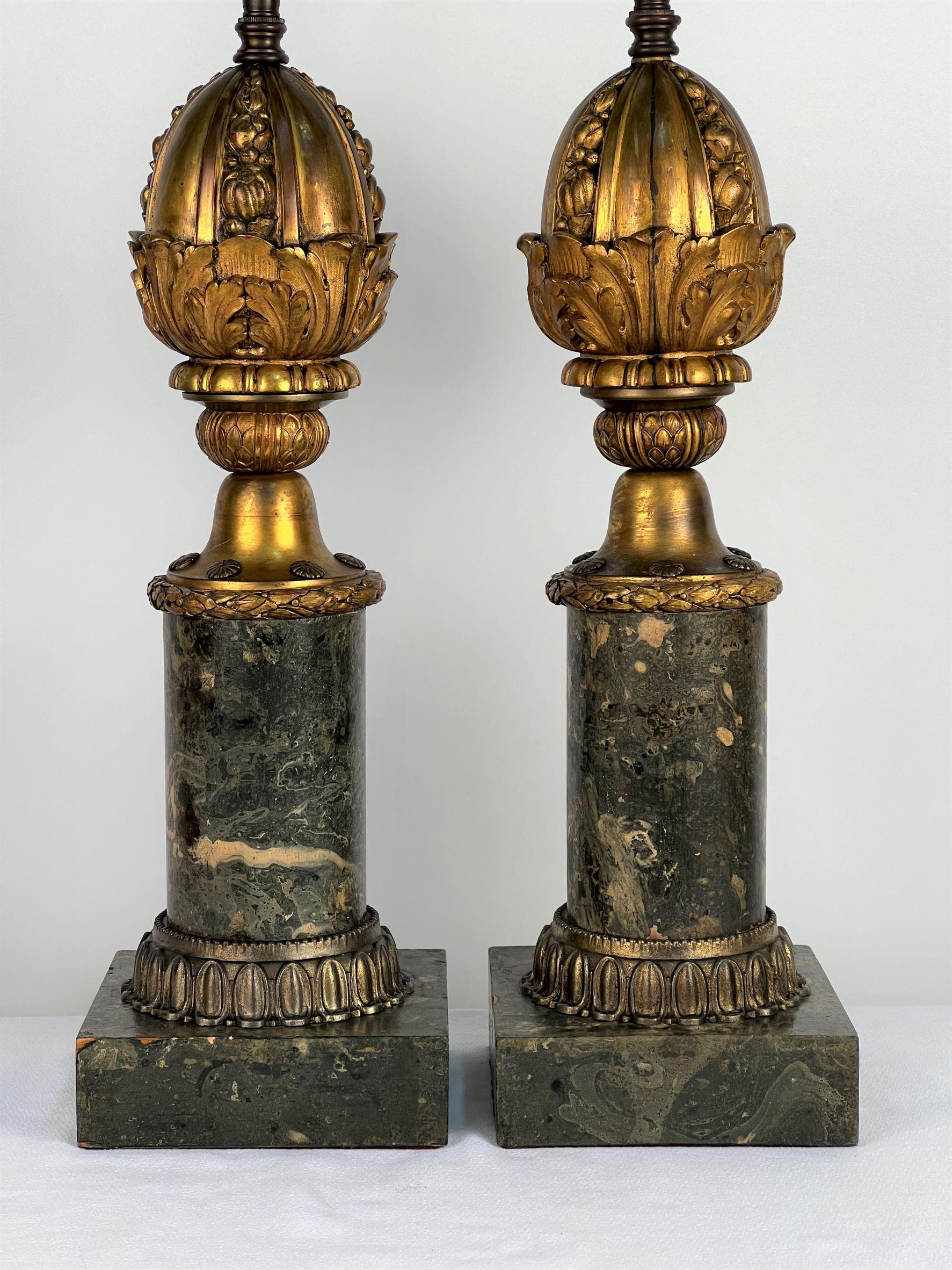 An exceptional pair of gilt cast bronze pomegranate shapes nestled in acanthus leaf cups mounted to faux marble pedestals ending in square faux marble basses. Decorative applied rosettes are mounted above laurel wreath bands. The faux marble has a