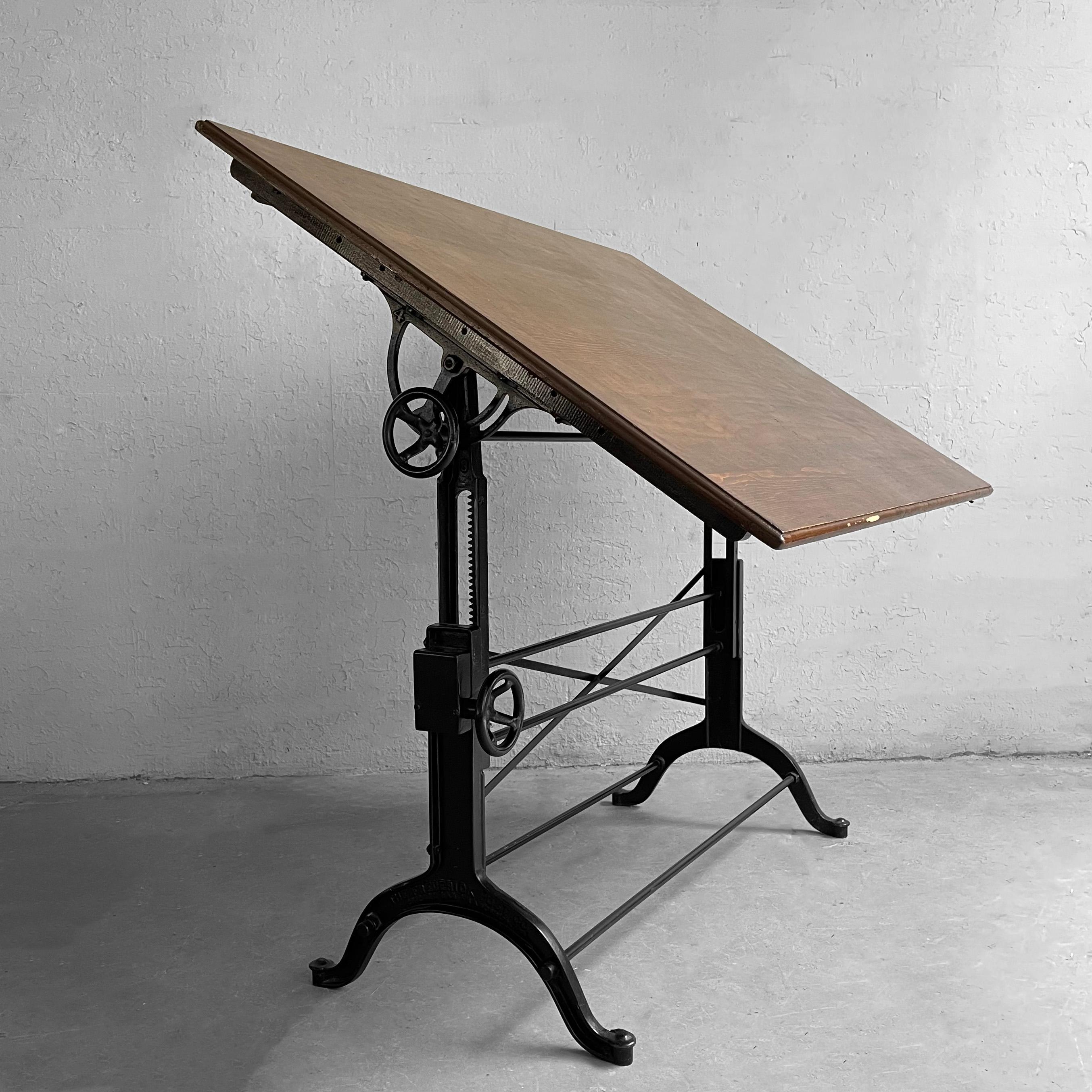 Early 20th century drafting table by the Frederick Post Co., features a stained maple top with 3 inch height storage drawer at the back and painted cast iron base. The table is height adjustable from 35-48 inches and tilt adjustable from almost