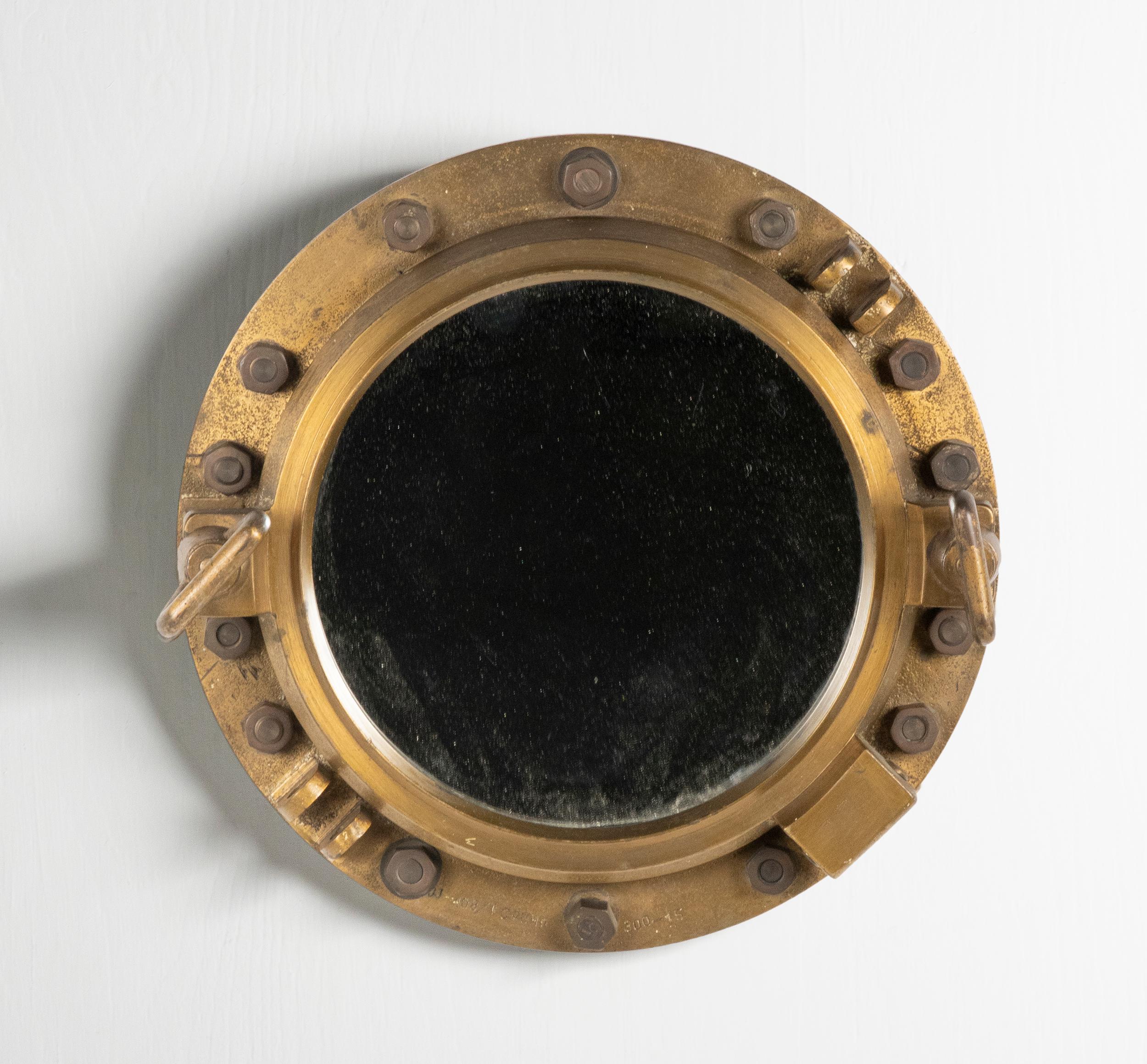 An antique heavy duty porthole made of cast iron. A mirror has been placed inside. The whole has a beautiful old patina, the copper-colored frame, and the original bolts. This maritime object was made around 1900-1920, origin unknown. The dimensions