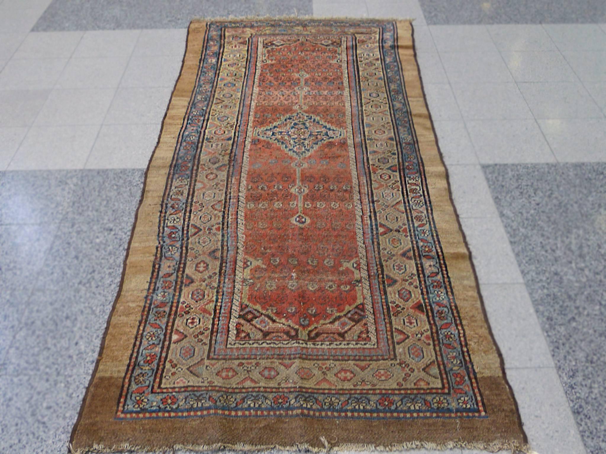 This Caucasian runner rug was handwoven in the 1900s. Its abrash and rich earth-toned palette includes pale yellows, pale reds, brown, ivory, and faded blues. The design consists of central medallion in a red rectangular field. In turn a series of