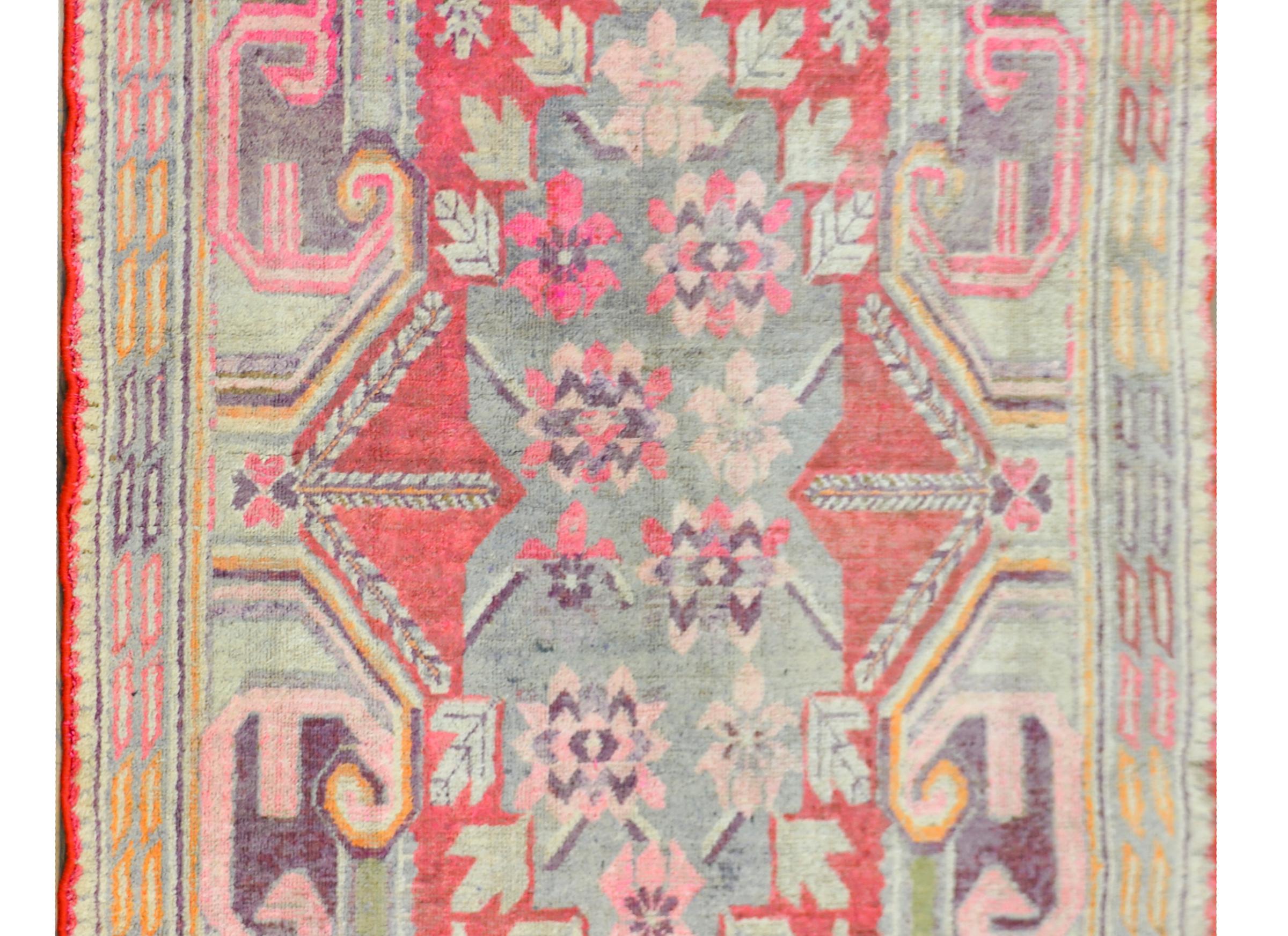 A striking early 20th century Central Asian Khotan rug with wonderful large-scale flowers and scrolling baroque ornamentations, all woven in beautiful muted greens, golds, reds, and violets.