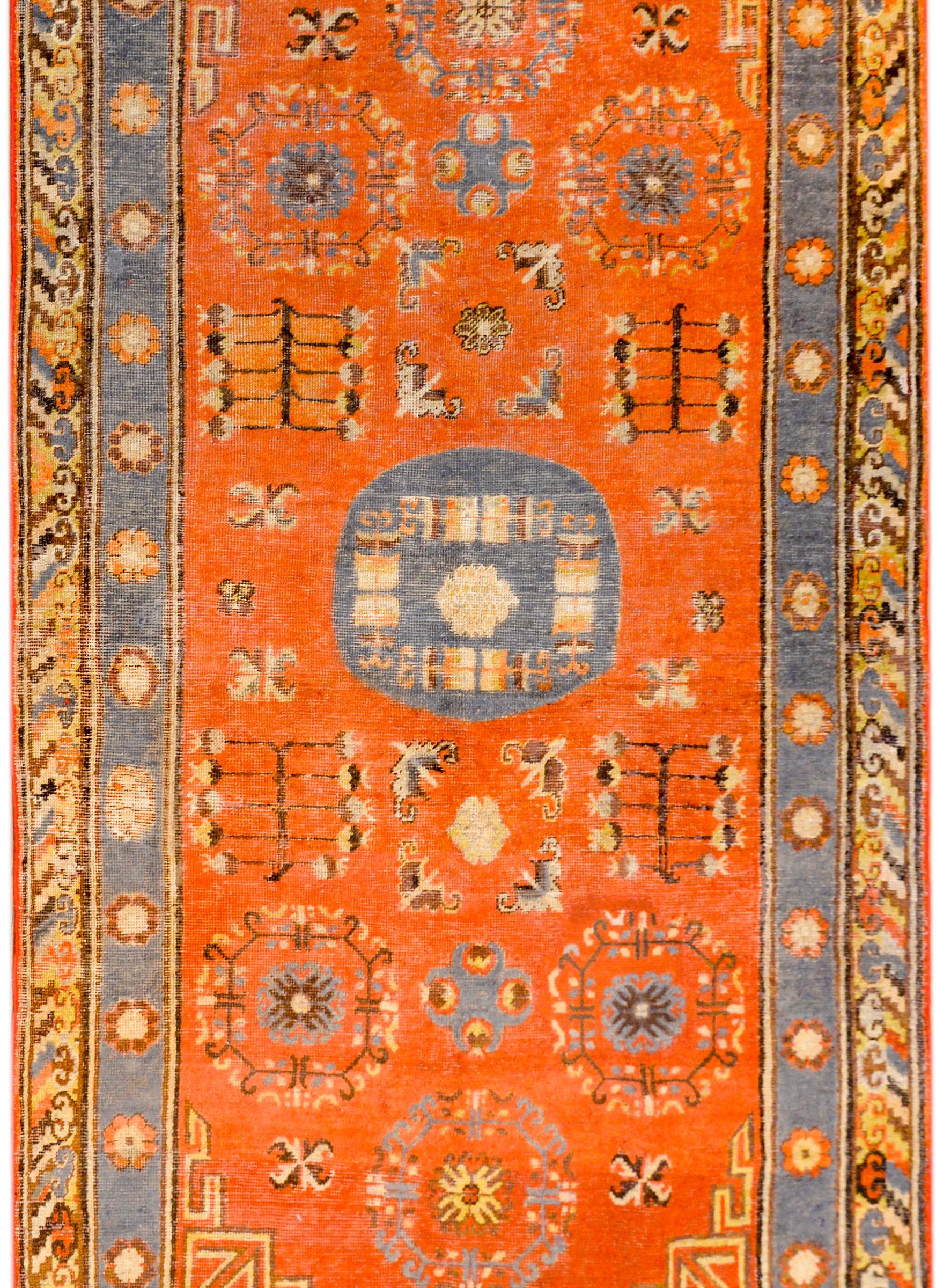 A fantastic early 20th century Central Asian Khotan rug with a beautiful pattern containing a field of stylized flowers and flowering trees-of-life on a brilliant orange colored background. The border is gorgeous, with an inner floral stripe on a