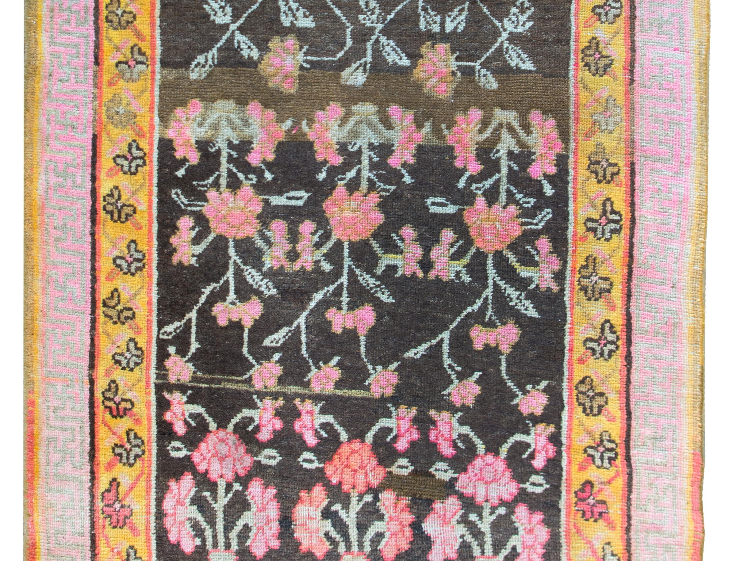 A charming and whimsical early 20th century Central Asian Khotan Rug with an all-over pink peony pattern with two larger peonies at the bottom. The border is sweet with a petite floral and scrolling vine patterned inner border and a meandering motif