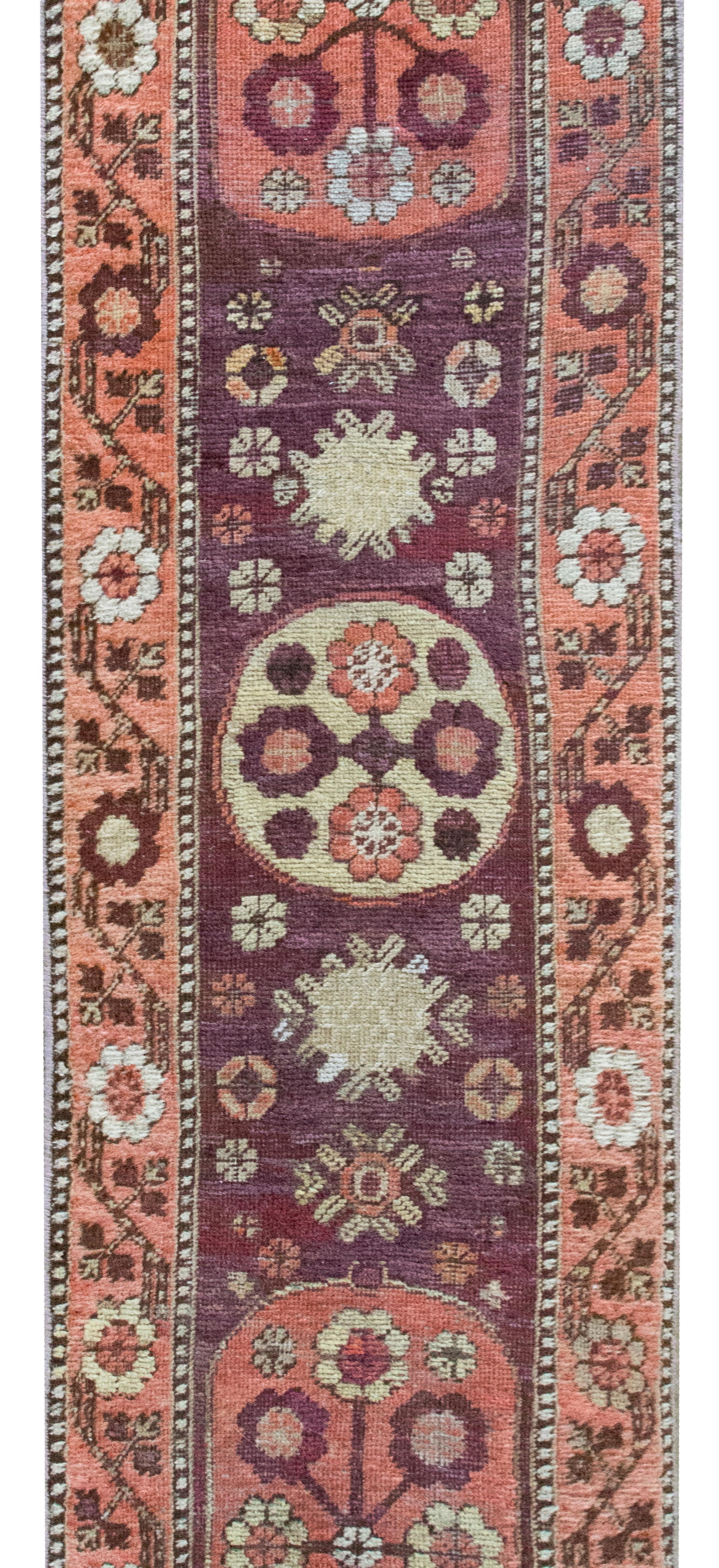 Un delizioso piccolo runner Khotan dell'inizio del XX secolo con un motivo floreale a specchio che contiene tre medaglioni di flora in un campo di fiori ancora più stilizzati, circondato da un bordo con fiori dello stesso stile e viti che scorrono,