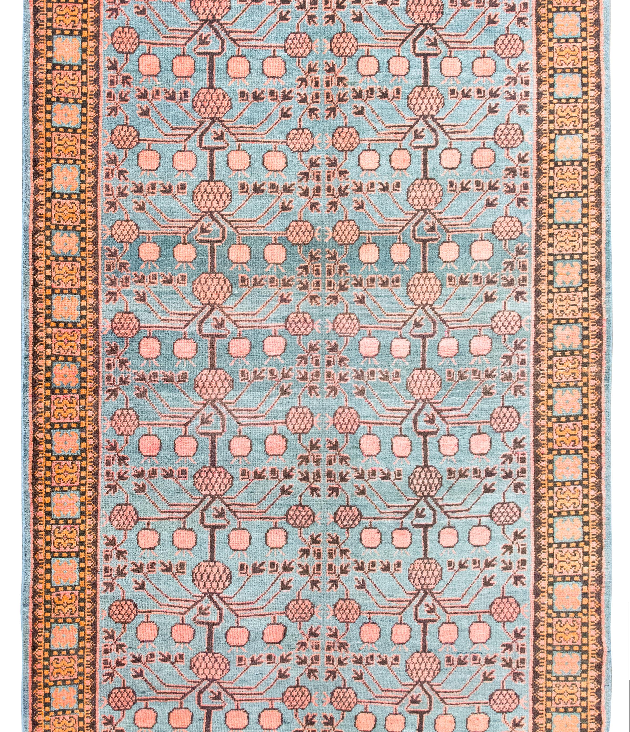 Magnifique Khotan d'Asie centrale du début du 20e siècle, avec un motif de grenade stylisé sur un fond indigo, entouré d'une bordure à motif floral stylisé, le tout tissé en laine orange, cramoisie pâle et indigo.