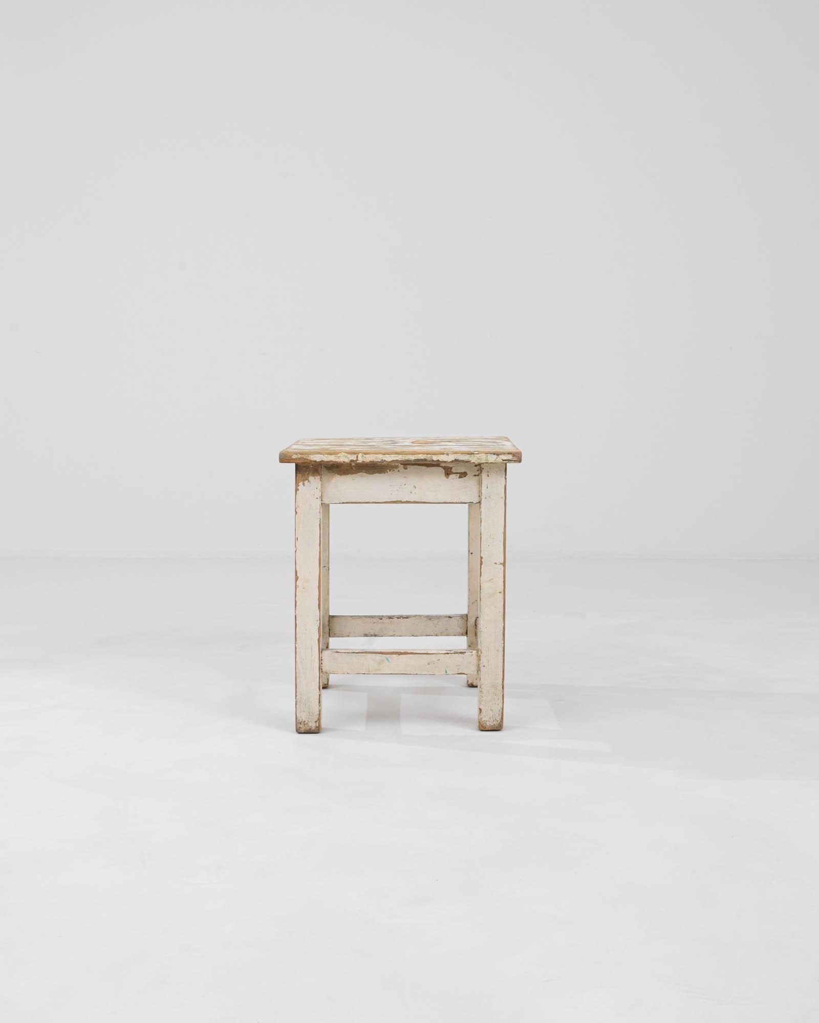 This Early 20th Century Central European stool captures the essence of a bygone era with its richly patinated wood and chipped paint finish. Each mark and scratch on its surface narrates the tale of its long-standing service and adds to its unique