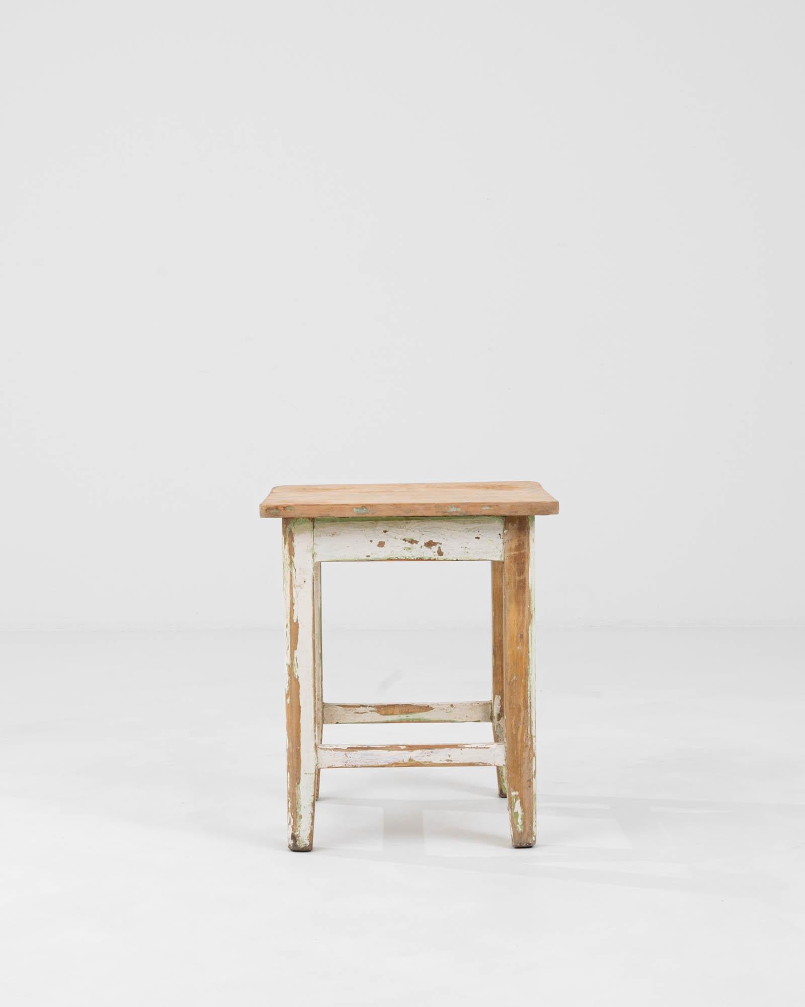 Embrace the essence of rustic charm with this Early 20th Century Central European wood patinated stool. Its storied life is evident in the layers of paint that suggest years of use, each mark and scratch a narrative of its past. Crafted with