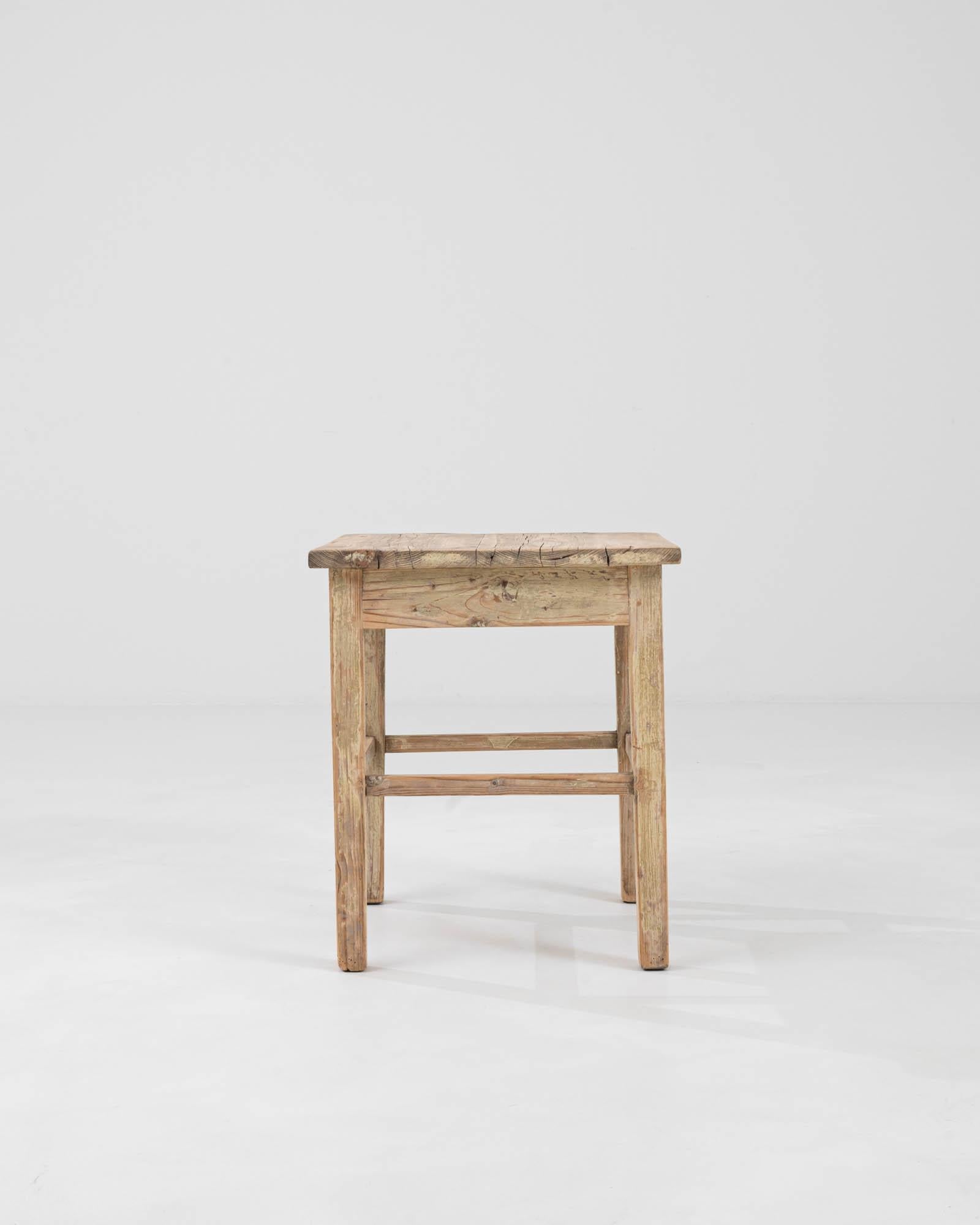This Early 20th Century Central European wood patinated stool is a testament to the timeless beauty and durability of artisanal craftsmanship. Its raw and natural finish highlights the authentic wood grains and character marks, imbuing this piece